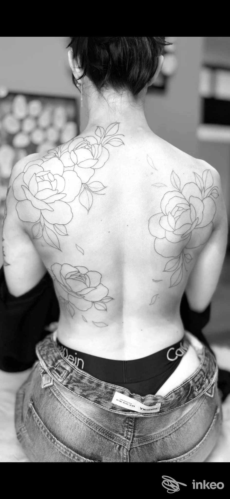 Tatouaggi floreali delineati sulla schiena di una persona, viso non visibile, foto in bianco e nero.