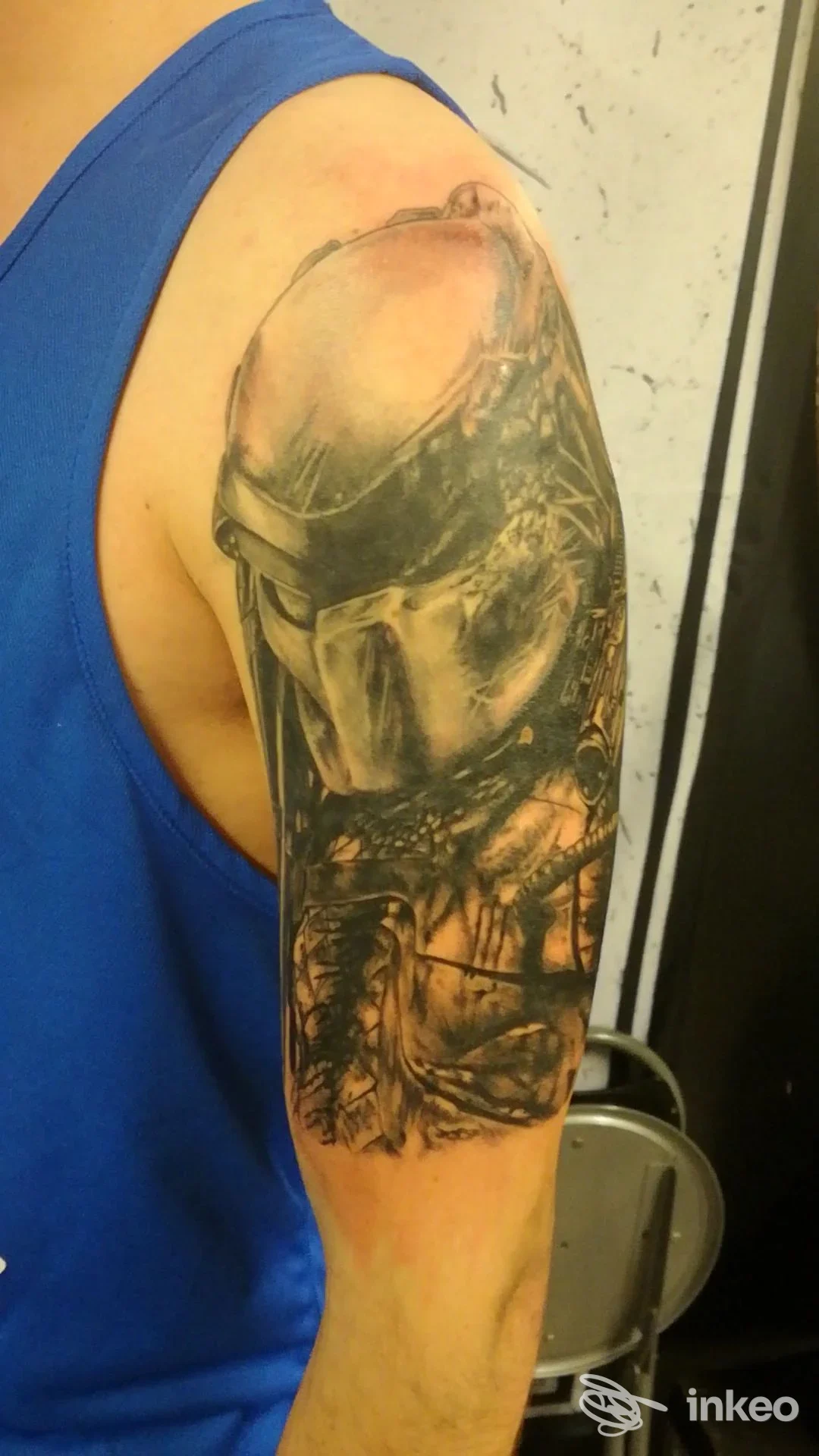 Tattoo realistico su braccio sinistro: figura di casco o maschera scura incisa sulla pelle, con dettagli e ombre. Nessun volto visibile; nessuna sovrapposizione sociale o schermo.