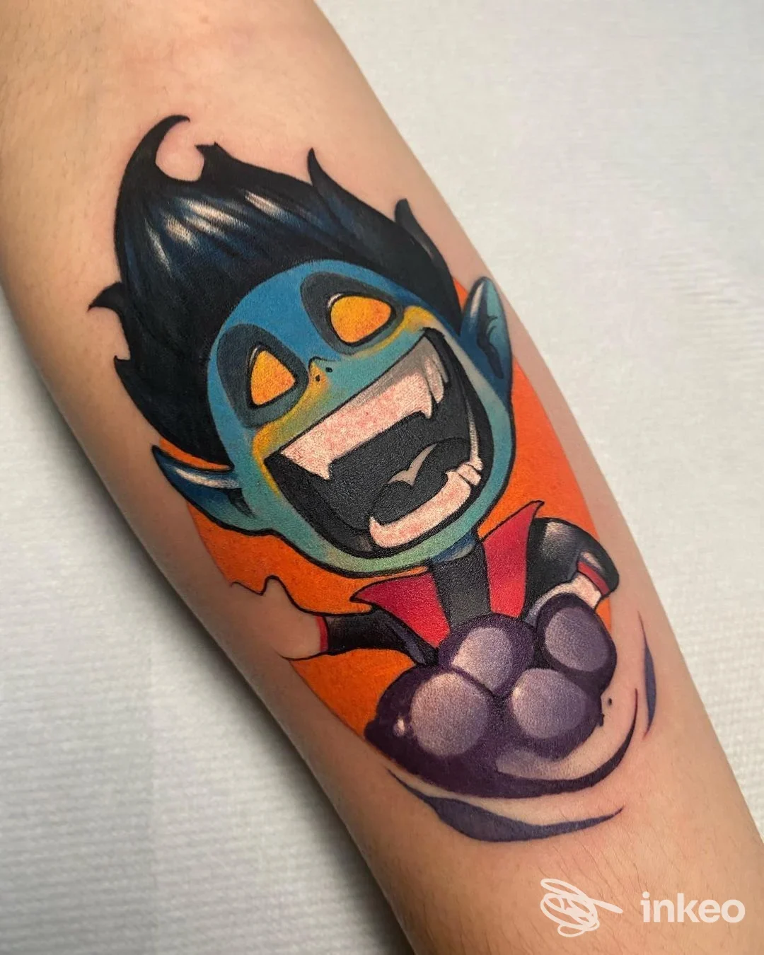 Tatuaggio colorato su avambraccio raffigurante un personaggio cartoonesco con espressione felice, sfondo arancione. Nulla di testo o logo visibile.