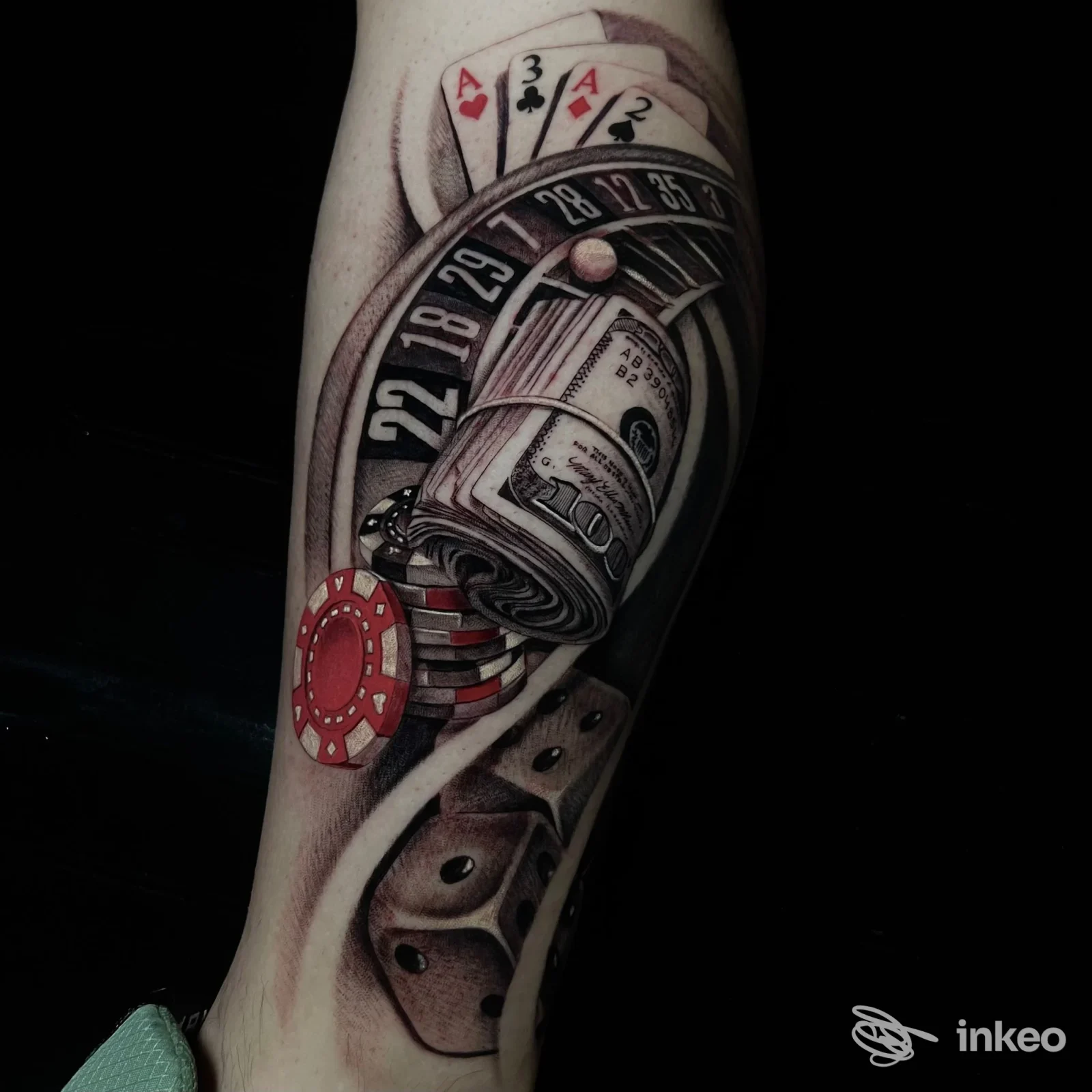 Tattoo sull'avambraccio che mostra una ruota della roulette, fiches e carte da poker con tonalità scure, realizzazione su pelle reale.
