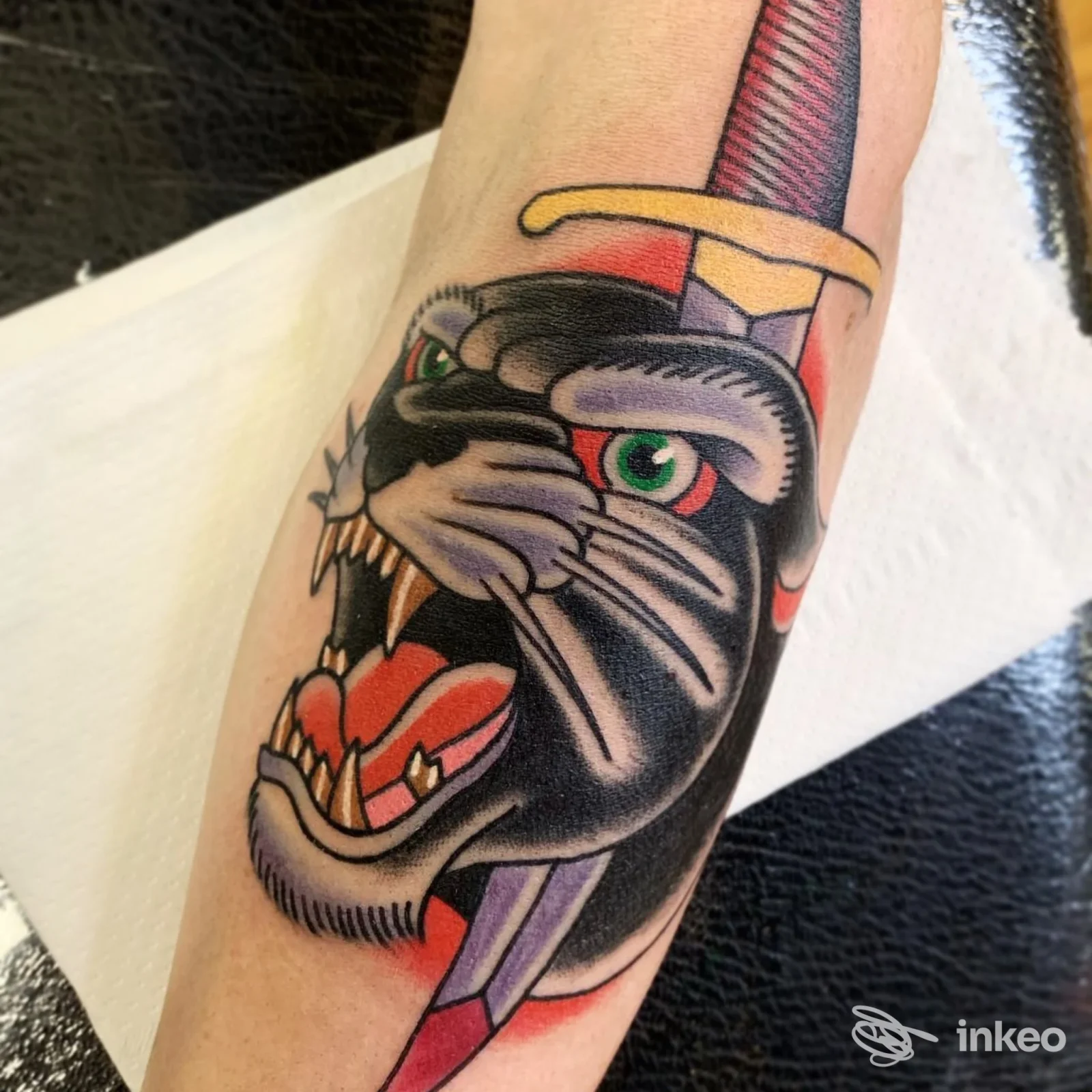 Tatuaggio a colori su pelle raffigurante una creatura con cappello, con zanne e occhi verdi, visibile sull’avambraccio.