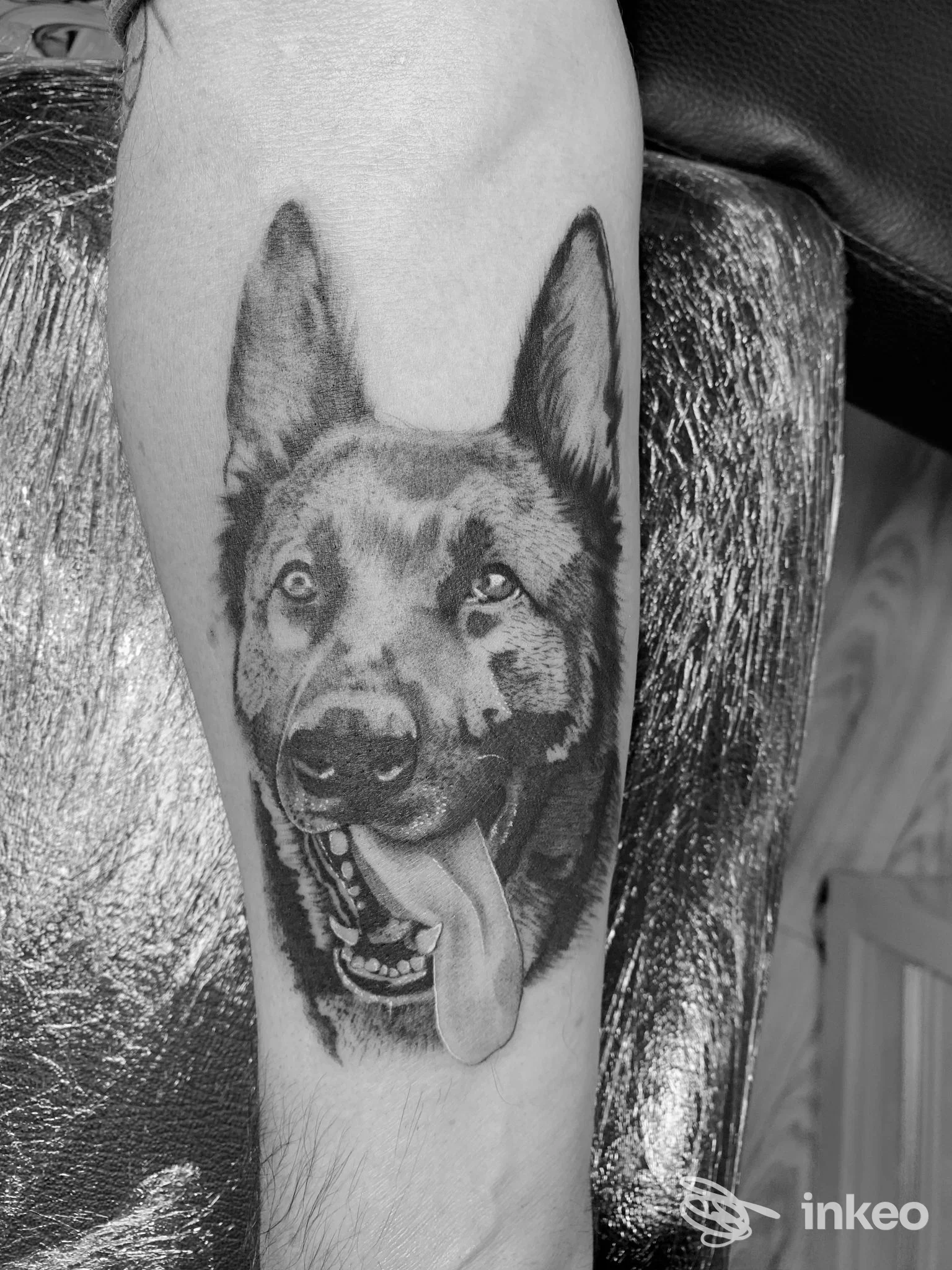 Tattoo realistico di una testa di cane sul braccio, in bianco e nero, con lingua pendente.