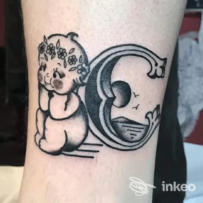 Tattoo raffigurante un cucciolo con corona di fiori accanto a una grande lettera C stilizzata, su pelle chiara, realizzato da Old Ways Tattoo, Melzo