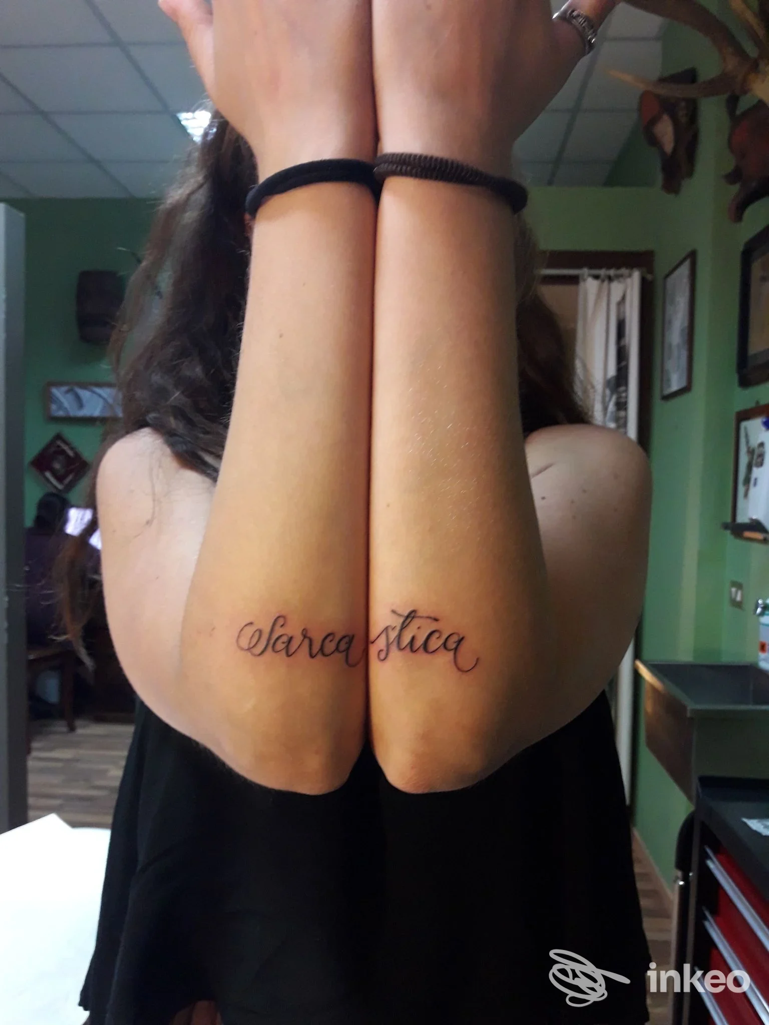 Due avambracci incrociati con un tatuaggio in corsivo visibile sulla pelle, illuminazione neutra e sfondo di studio.