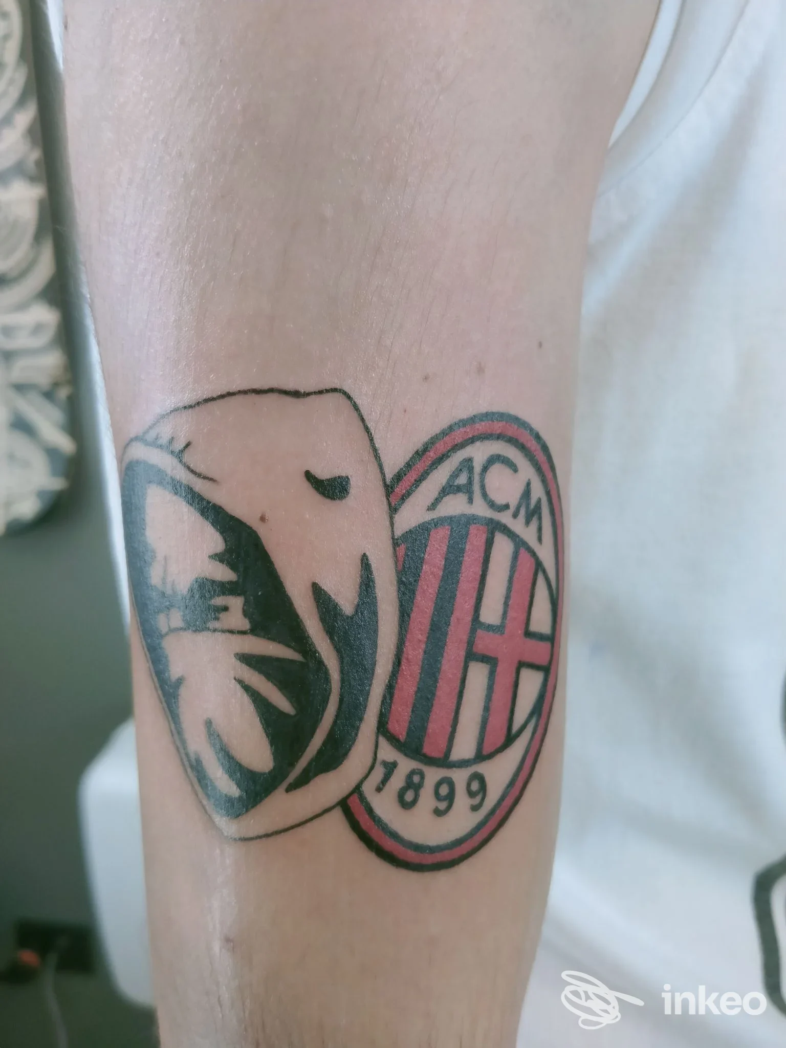 Tattoo sull'avambraccio che mostra una figura stilizzata a forma di dente accanto al logo rotondo dell'AC Milan, con colori nero/blu e rosso.