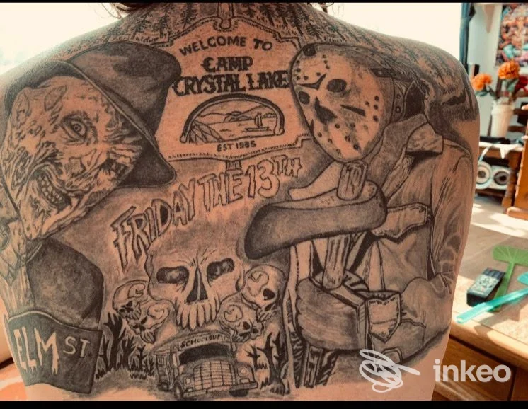 Schiena di una persona con numerosi tatuaggi scuri e dettagliati: volti, simboli e scene con stile tradizionale, senza persone illuminate frontalmente.