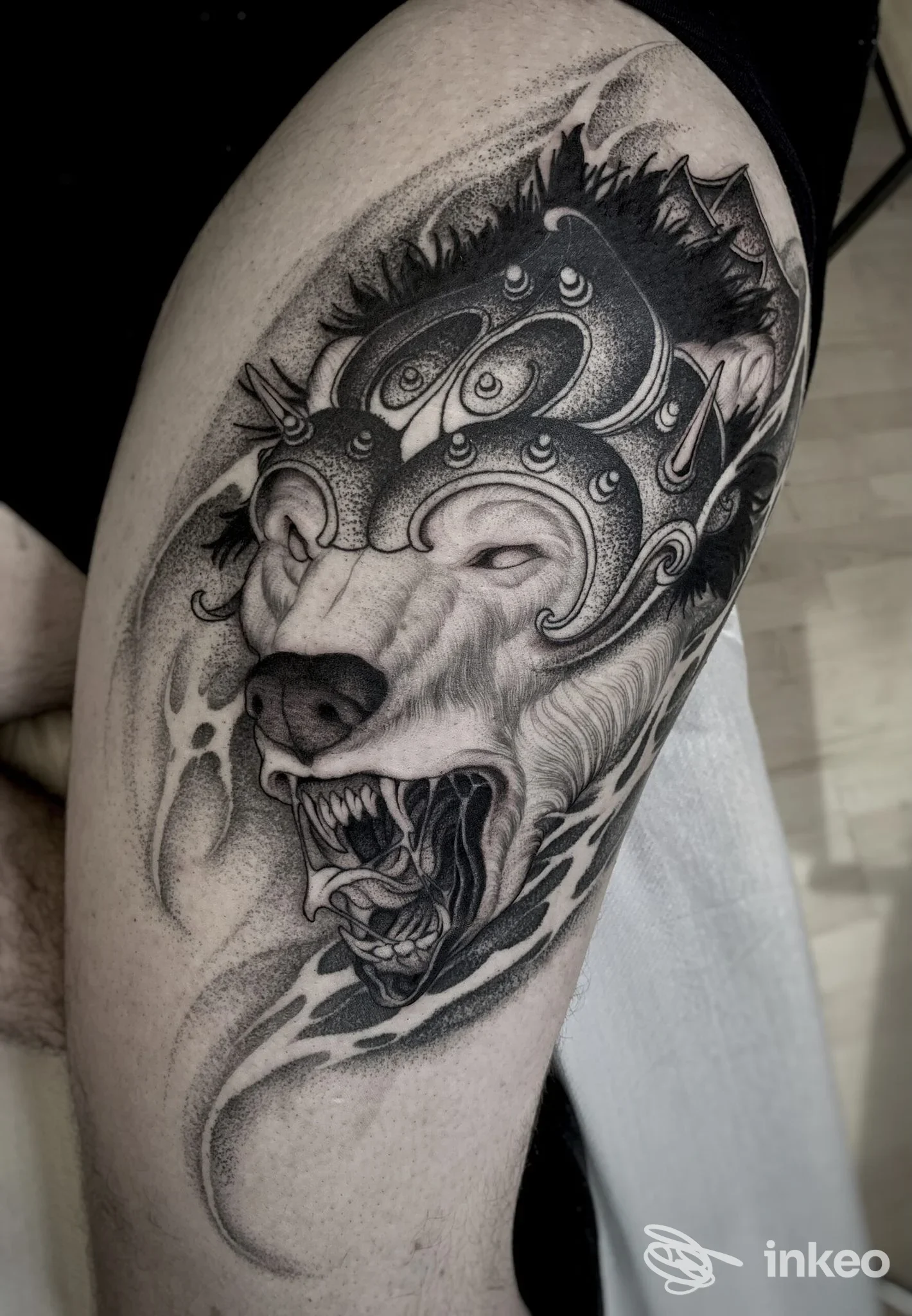 Tattoo realistico su braccio superiore: ritratto di lupo con ornamenti in bianco e nero su pelle umana, scatto laterale senza volto visibile.
