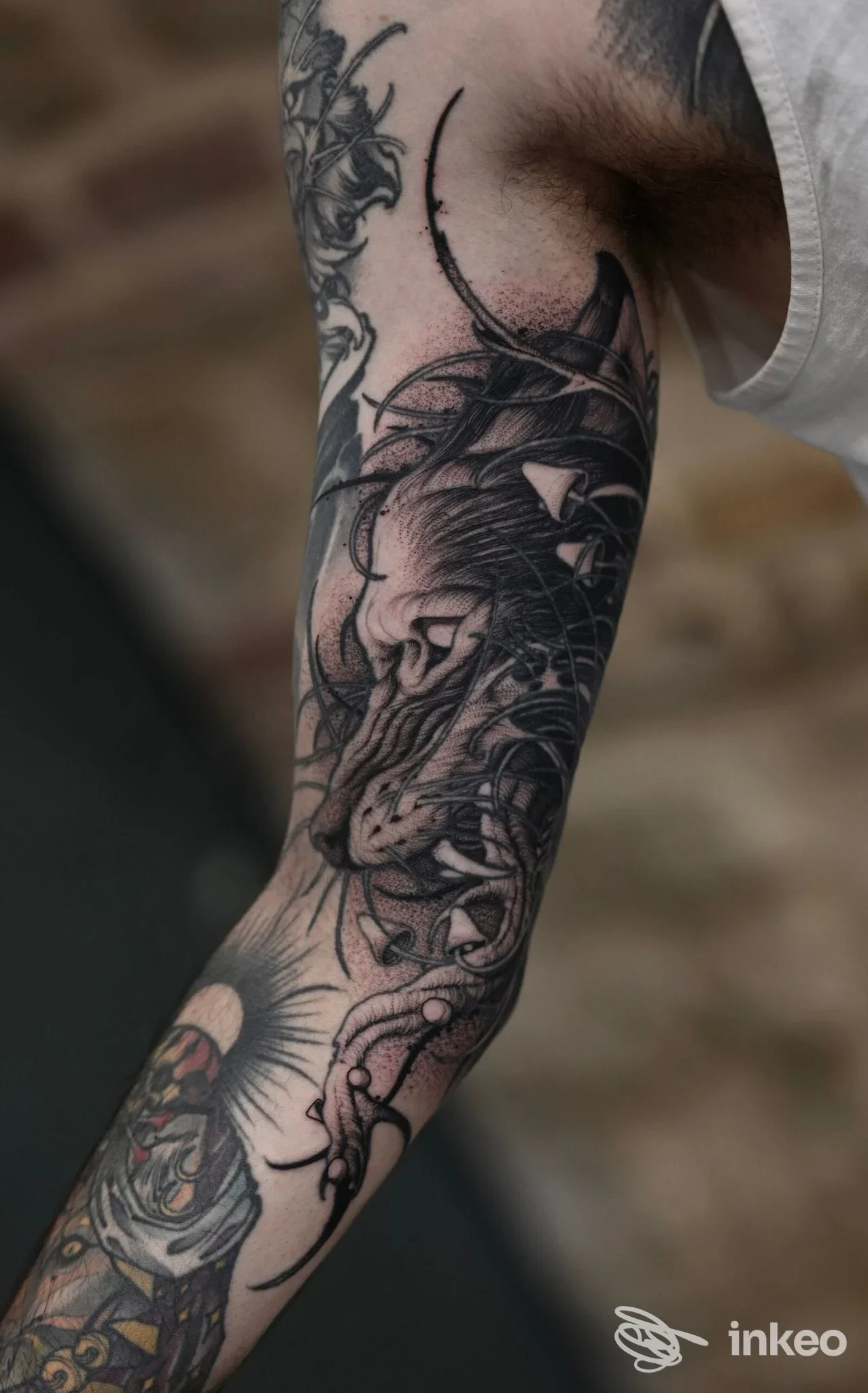 Tatuaggio in bianco e nero su braccio, disegno dettagliato e lineare che si estende lungo la pelle, parzialmente visibile sotto una manica. Studio Angelo Barulli nella descrizione.