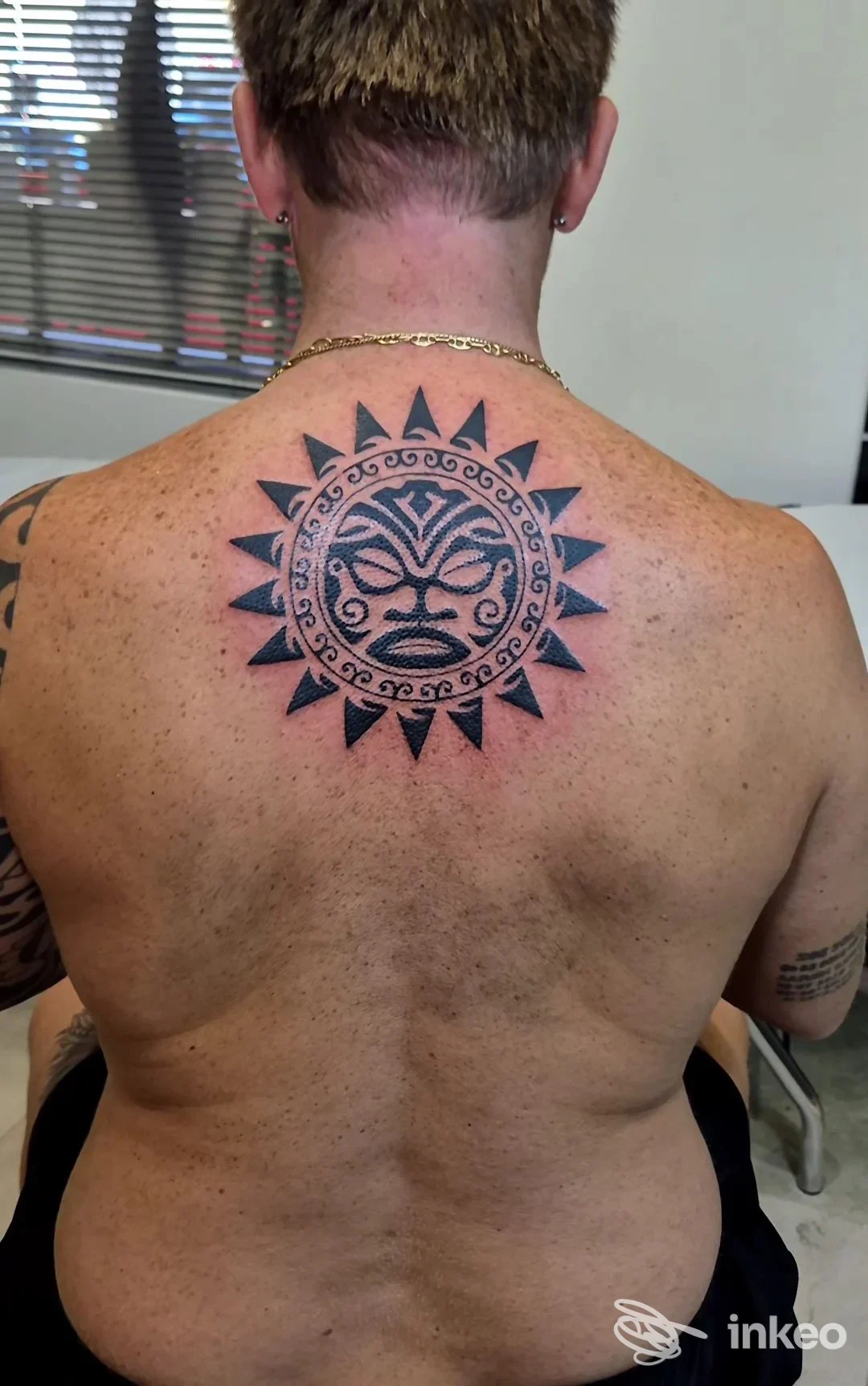 Tattoo circolare a sole con volto stilizzato al centro sulla schiena; raggi neri appuntiti circondano un motivo cerchiato.