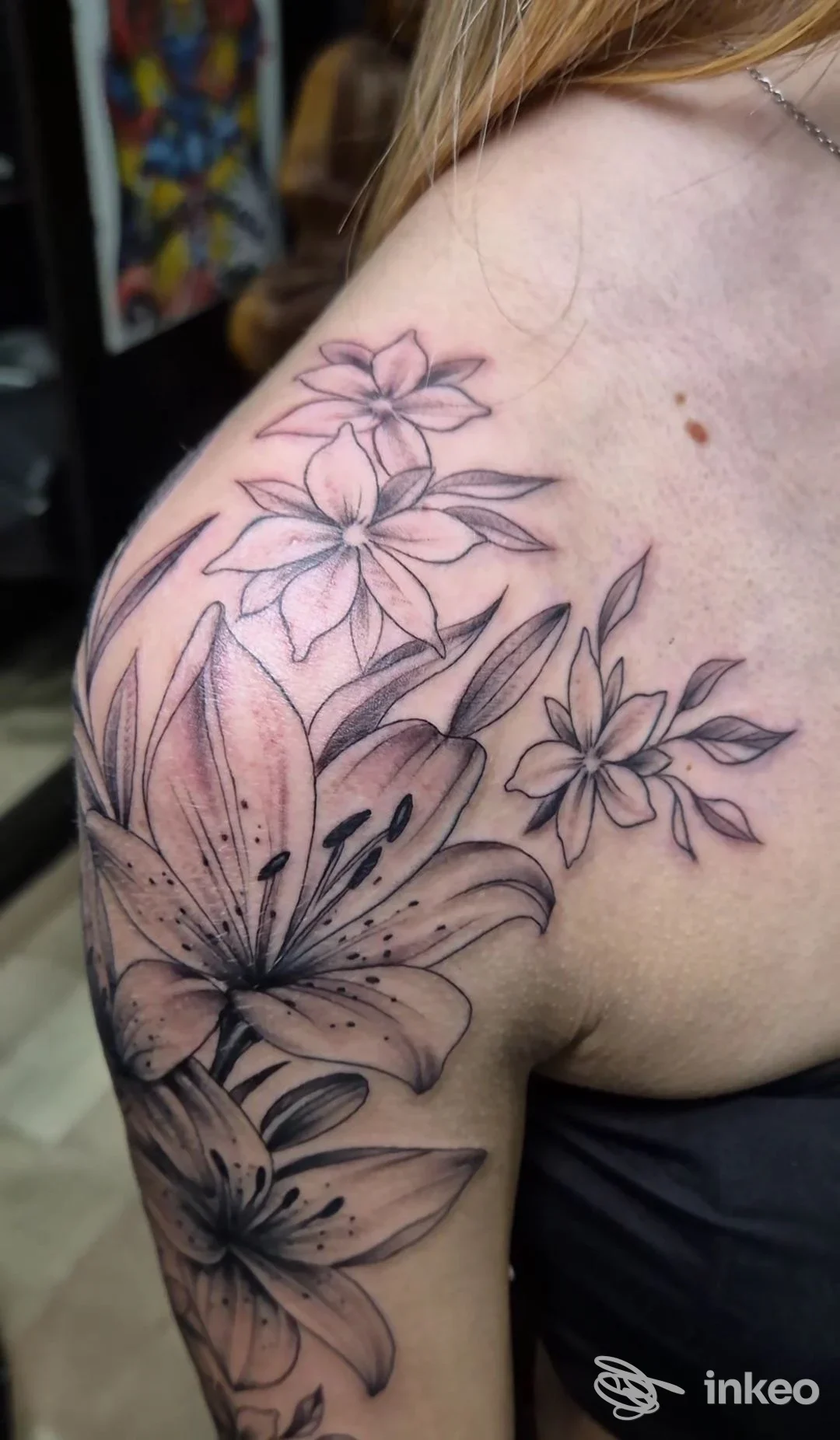Tattoo floreale su spalla e braccio di una persona, disegno in bianco e nero con dettagli di grandi fiori e petali, lato sinistro della spalla visibile.