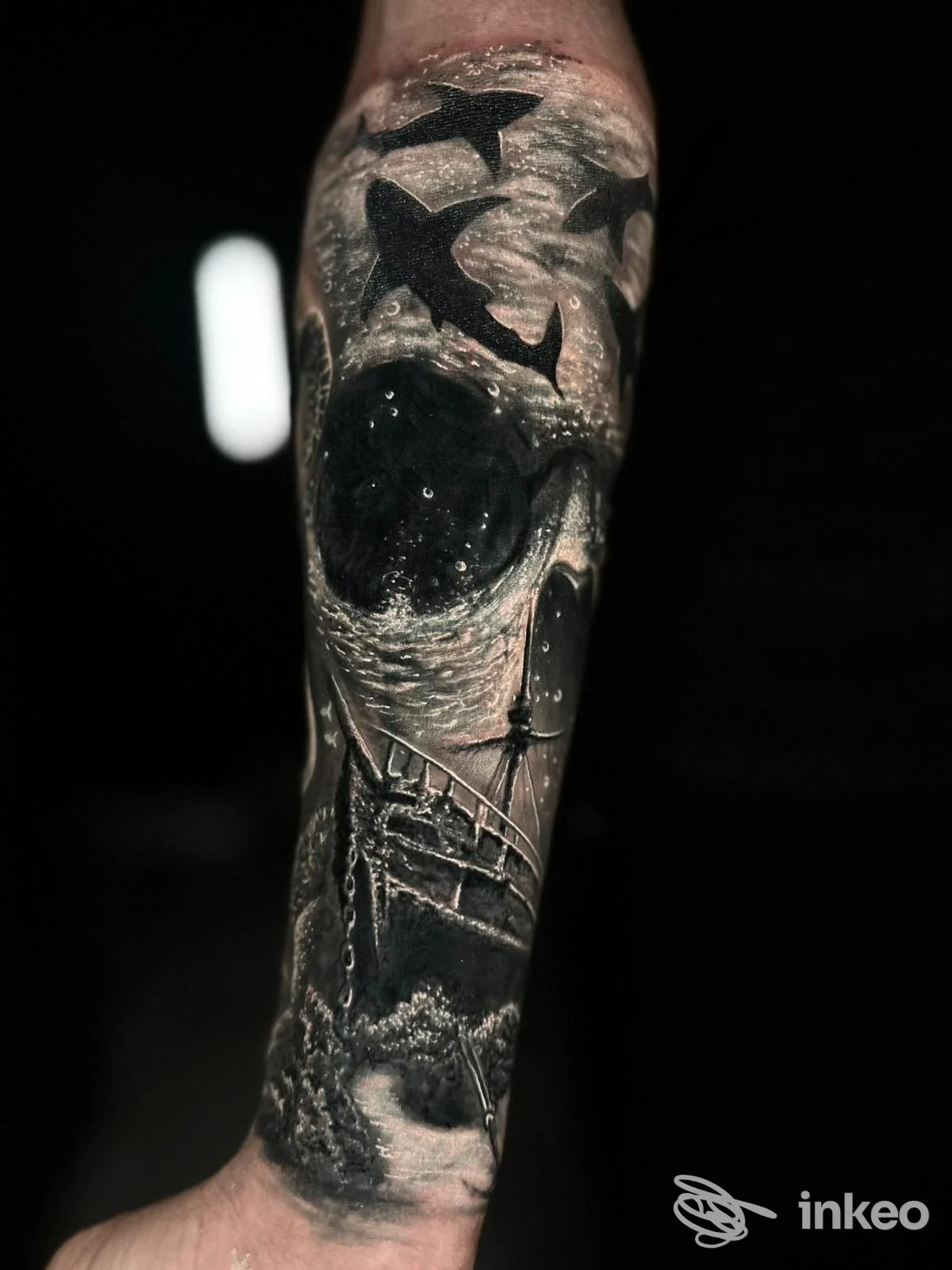 Tatuaggio in bianco e nero sull'avambraccio raffigurante uccelli in volo, cielo stellato e una scena marina con ponte, realizzato sulla pelle umana.