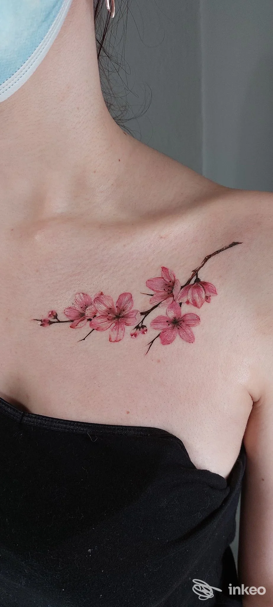 Tattoo floreale rosa lungo la clavicola di una persona, con delicate gemme fiorite su una pelle liscia, visibile in un decoltè scuro.