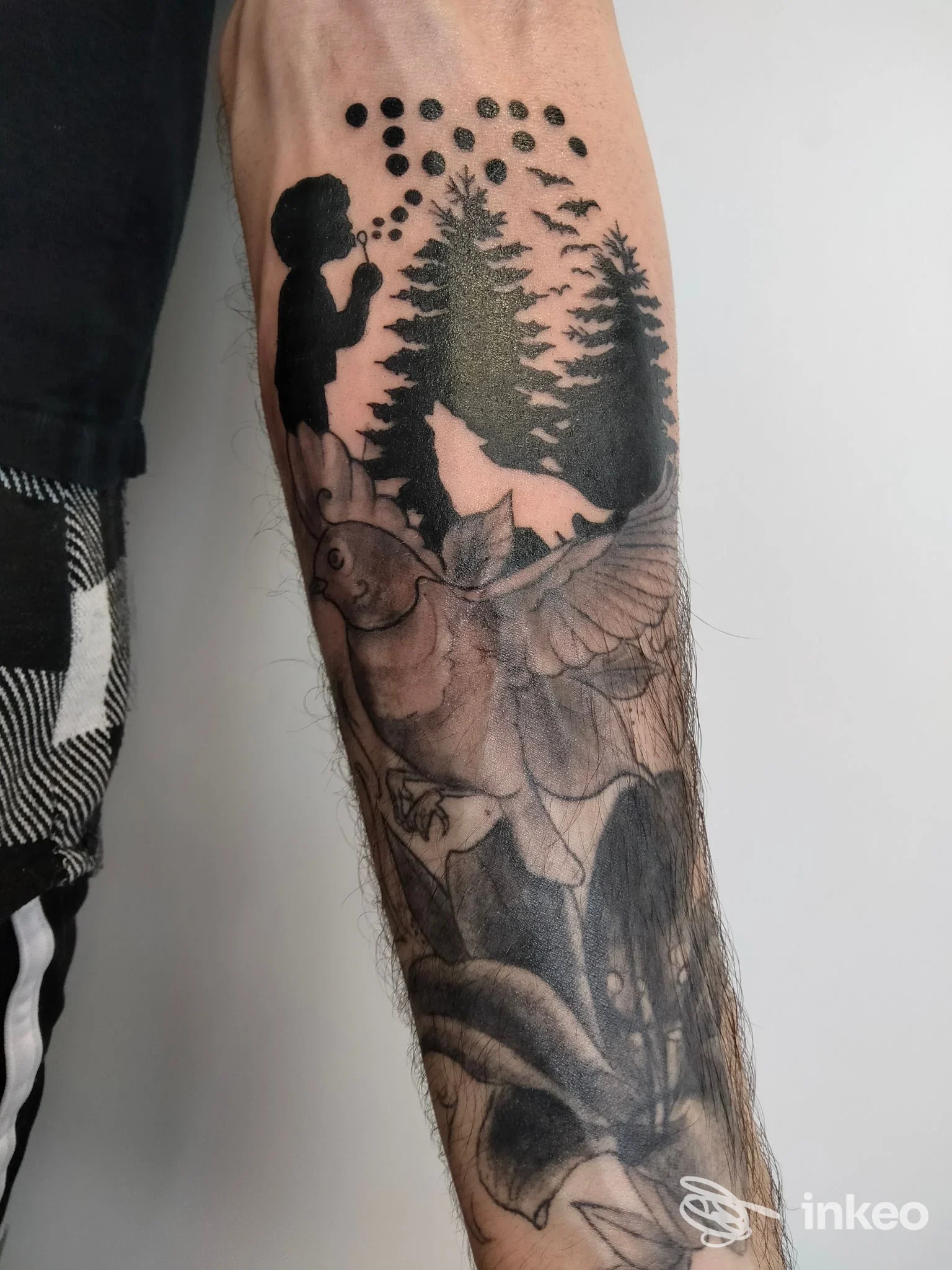 Tattoo sull’avambraccio raffigurante una scena boschiva con pini in silhouette e figure stilizzate, senza testo o elementi promozionali visibili.