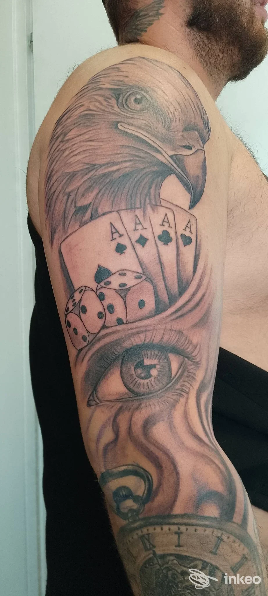 Tattoo sull'avambraccio: aquila in primo piano, insieme a carte da gioco, dadi e un occhio, su pelle reale; luce neutra, nessun overlay visivo.