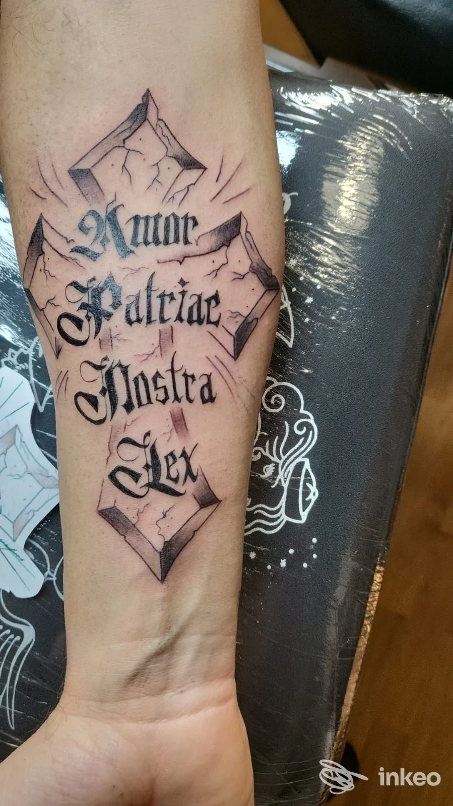 Tattoo sul polso sinistro con testo gotico e elementi decorativi geometrici, realizzato sulla pelle, nessun volto visibile.