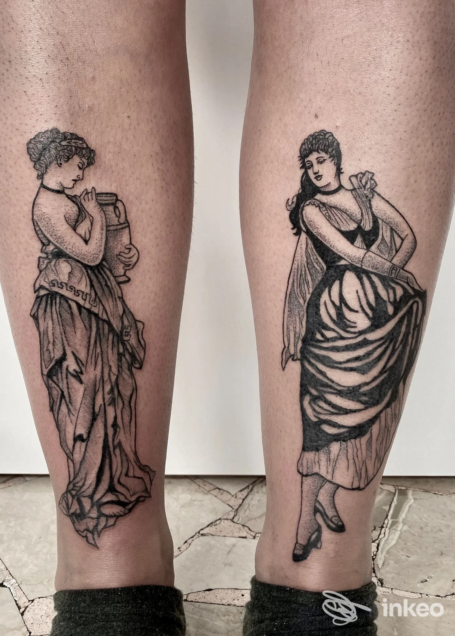 Due avambracci nudi mostrano tatuaggi di figure femminili in abiti d'epoca; i disegni raffigurano una donna a sinistra e una a destra, su entrambe le zone esterne delle braccia.