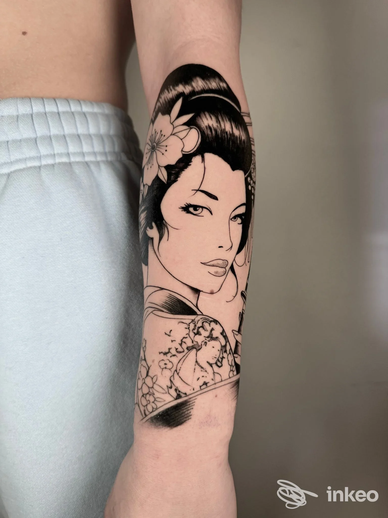 Tattoo in bianco e nero su avambraccio: ritratto femminile stilizzato tra motivi floreali, realizzato sulla pelle; foto singola senza watermark né overlay.
