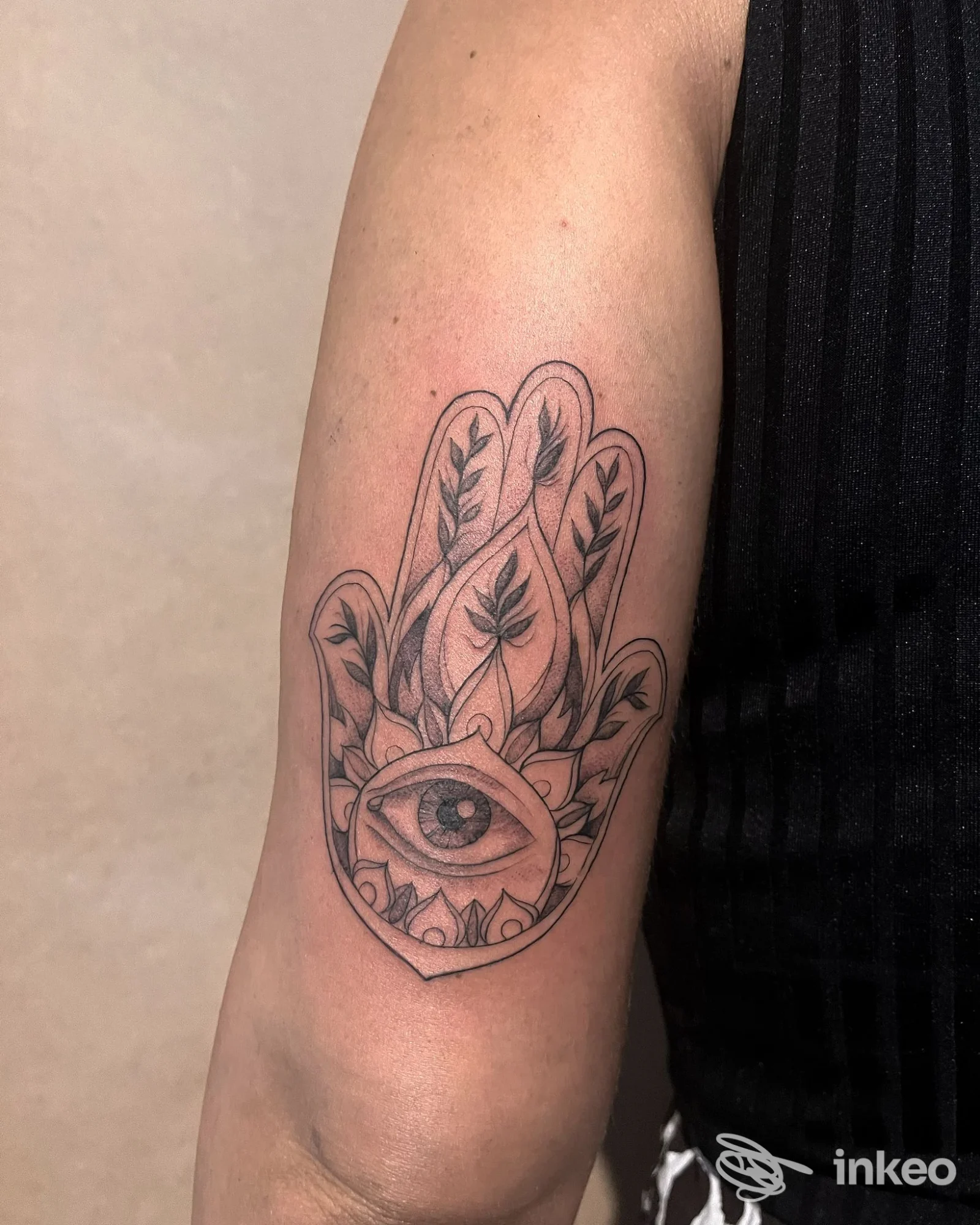 Tatuaggio lineare su avambraccio: una mano stilizzata con un occhio centrale, disegno in bianco e nero su pelle chiara.