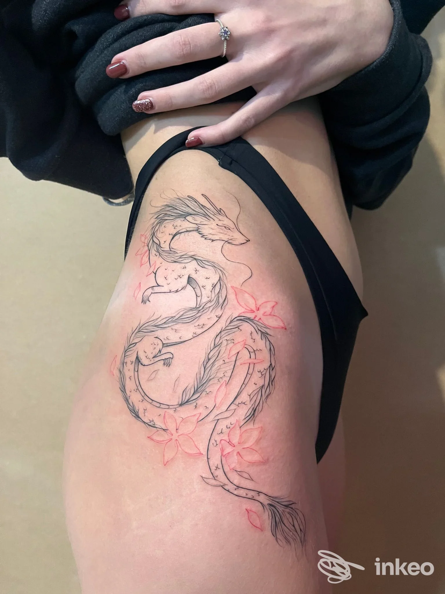 Scatto di una coscia femminile con tatuaggio in fase di realizzazione: linee nere di un drago, con leggeri accenni rossi, in attesa di riempimento; la persona indossa slip nero.