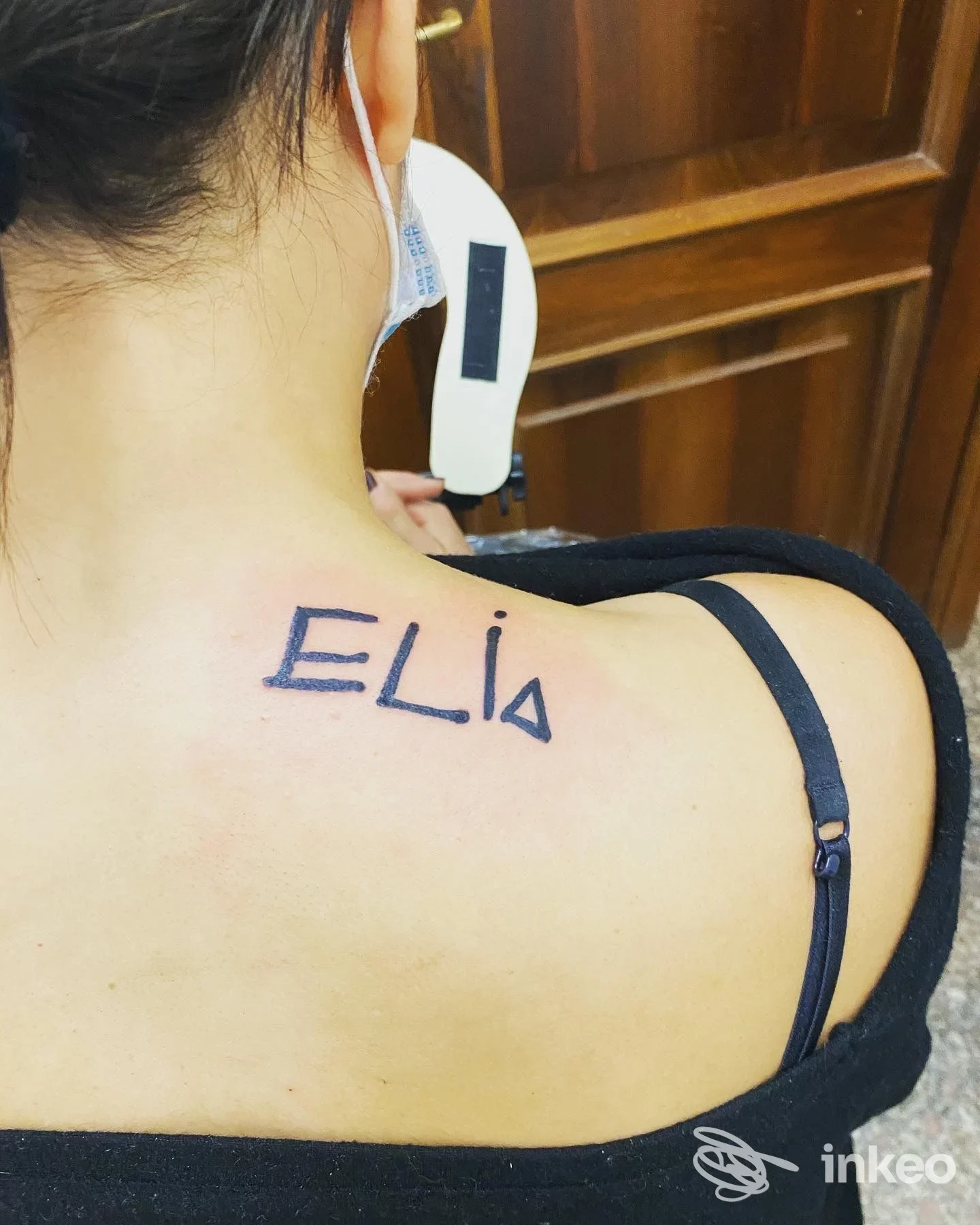 Tattoo sul dorso della spalla sinistra con la scritta ELIA in caratteri maiuscoli, visibile sulla pelle della persona.