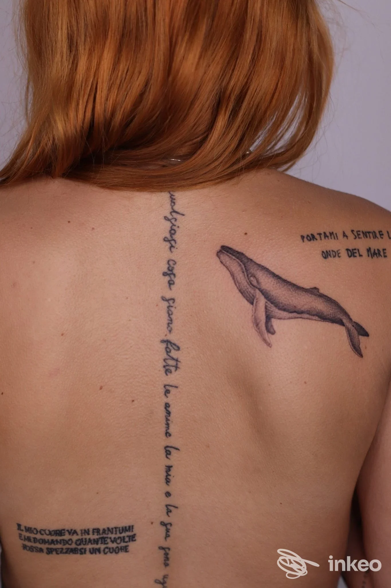 Tattoo sulla schiena di una persona, con una balena stilizzata che nuota e una scritta verticale lungo la colonna vertebrale.
