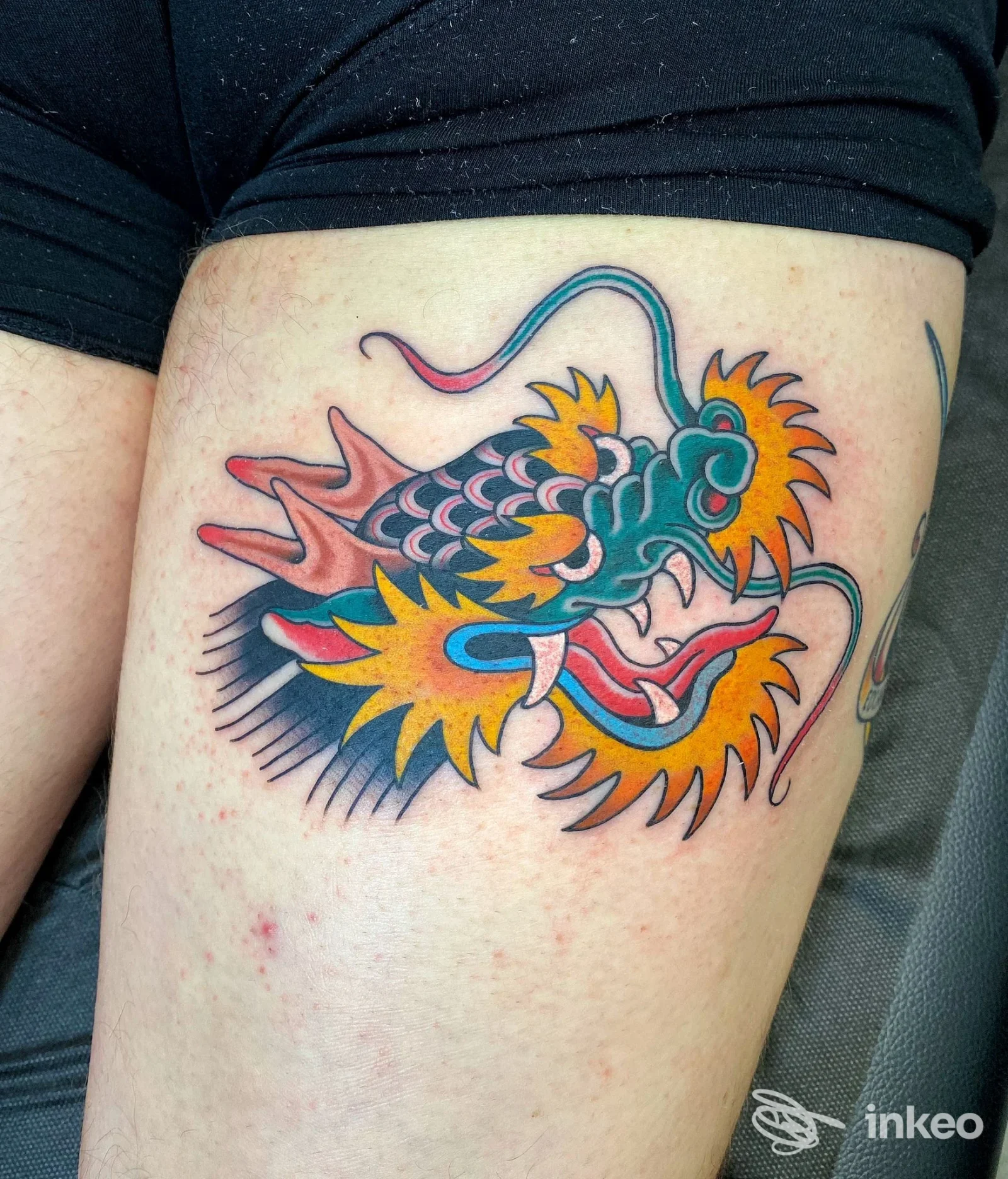 Tatuaggio colorato di drago stilizzato sulla coscia di una persona, visibile full volto assente.