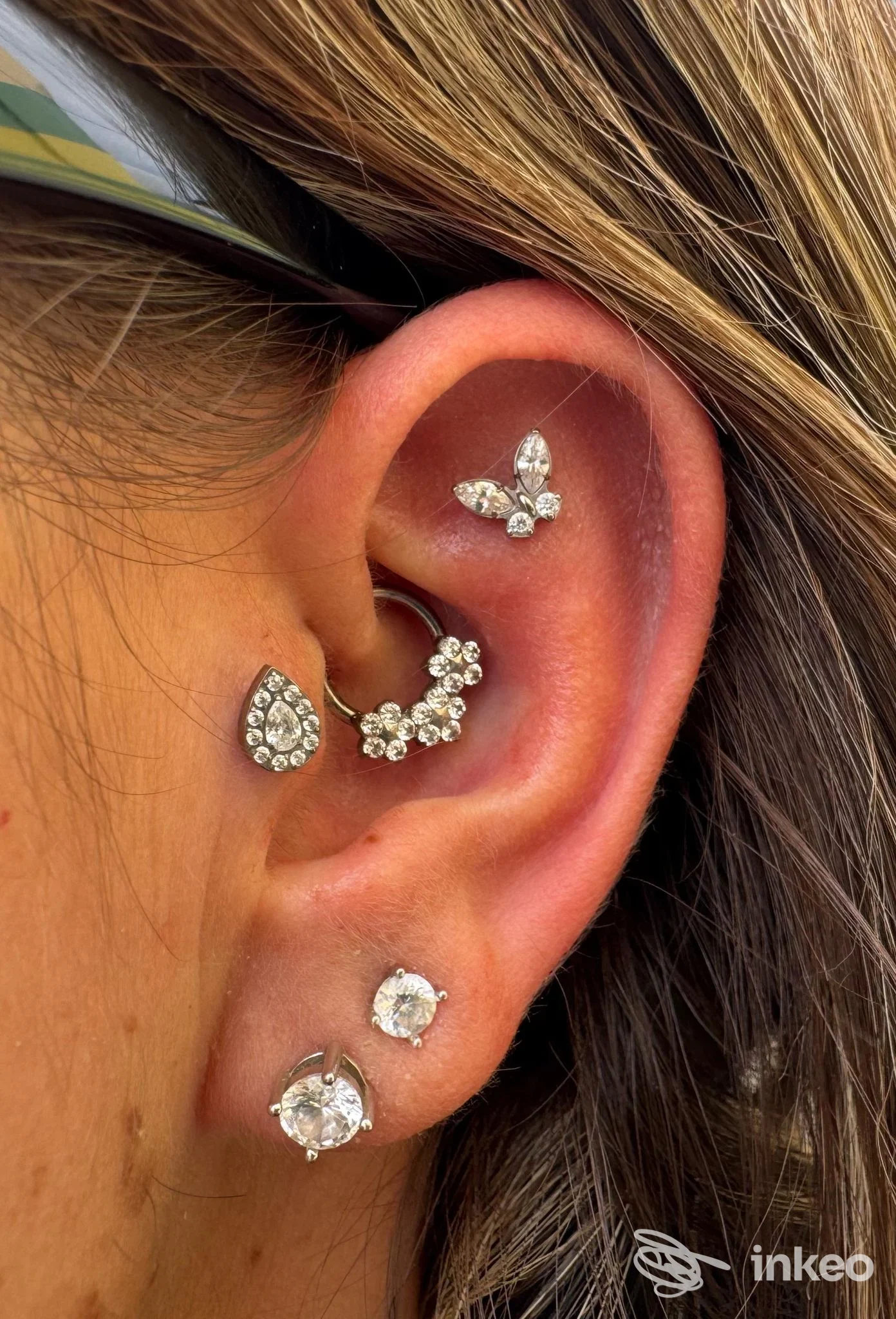 Orecchio sinistro con vari piercing gioiello a forma di goccia e barra curva, orecchini al lobo e al helix, gioielli brillanti su pelle.