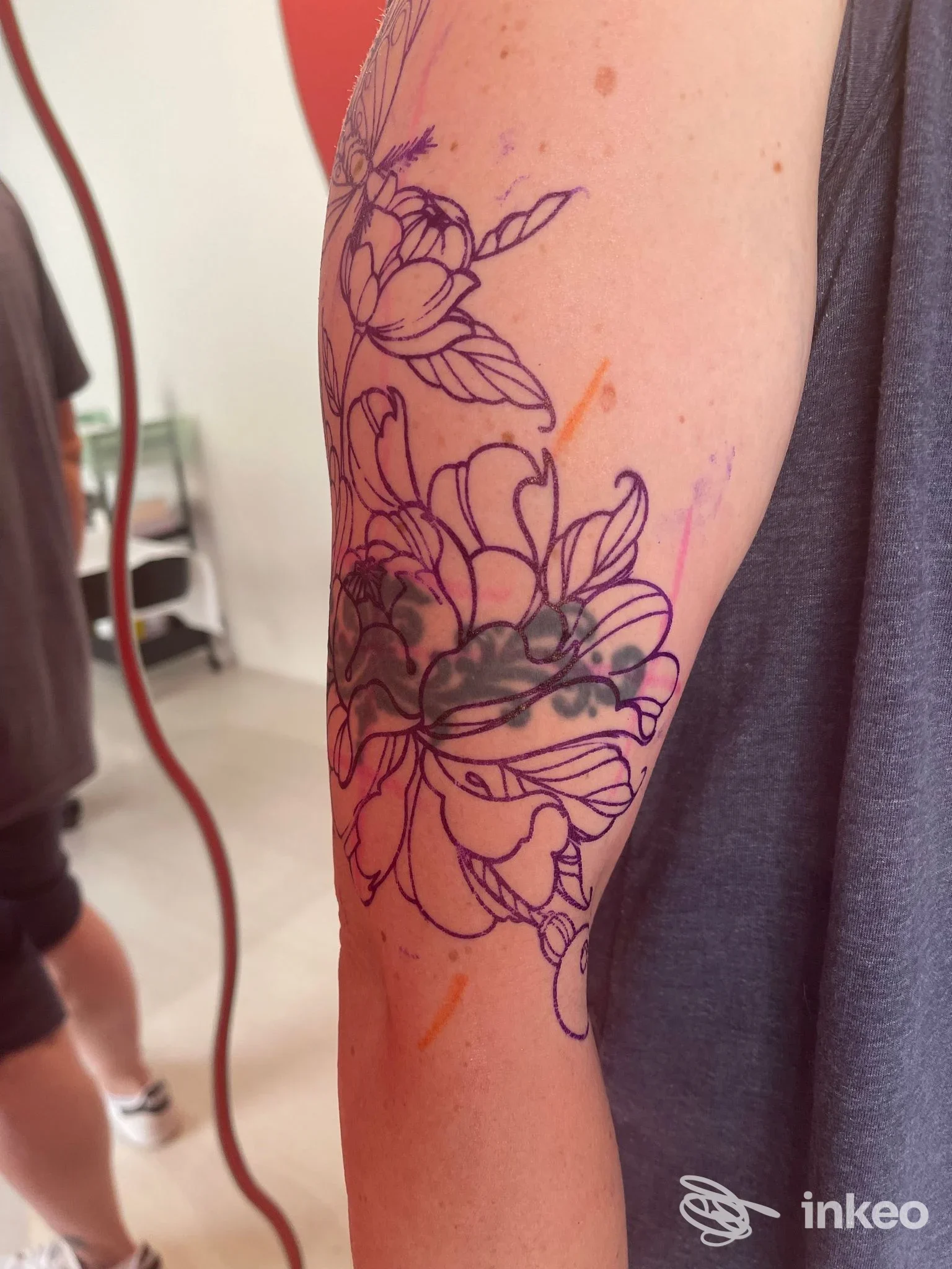 Tattoo sul braccio in fase di realizzazione, disegno a contorno di fiori con linee scure, senza viso visibile dell’utente.