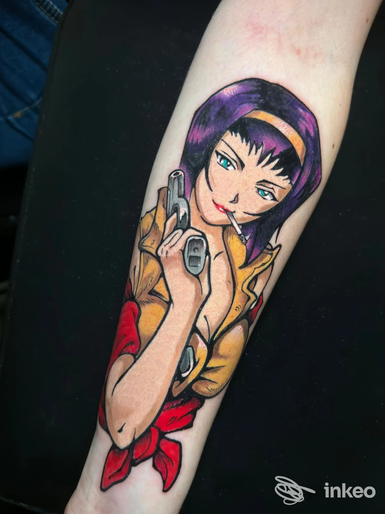 Tattoo colorato su avambraccio raffigurante una ragazza con capelli viola che brandisce una pistola e fuma, con sfondo giallo/rosso e una sciarpa rossa.