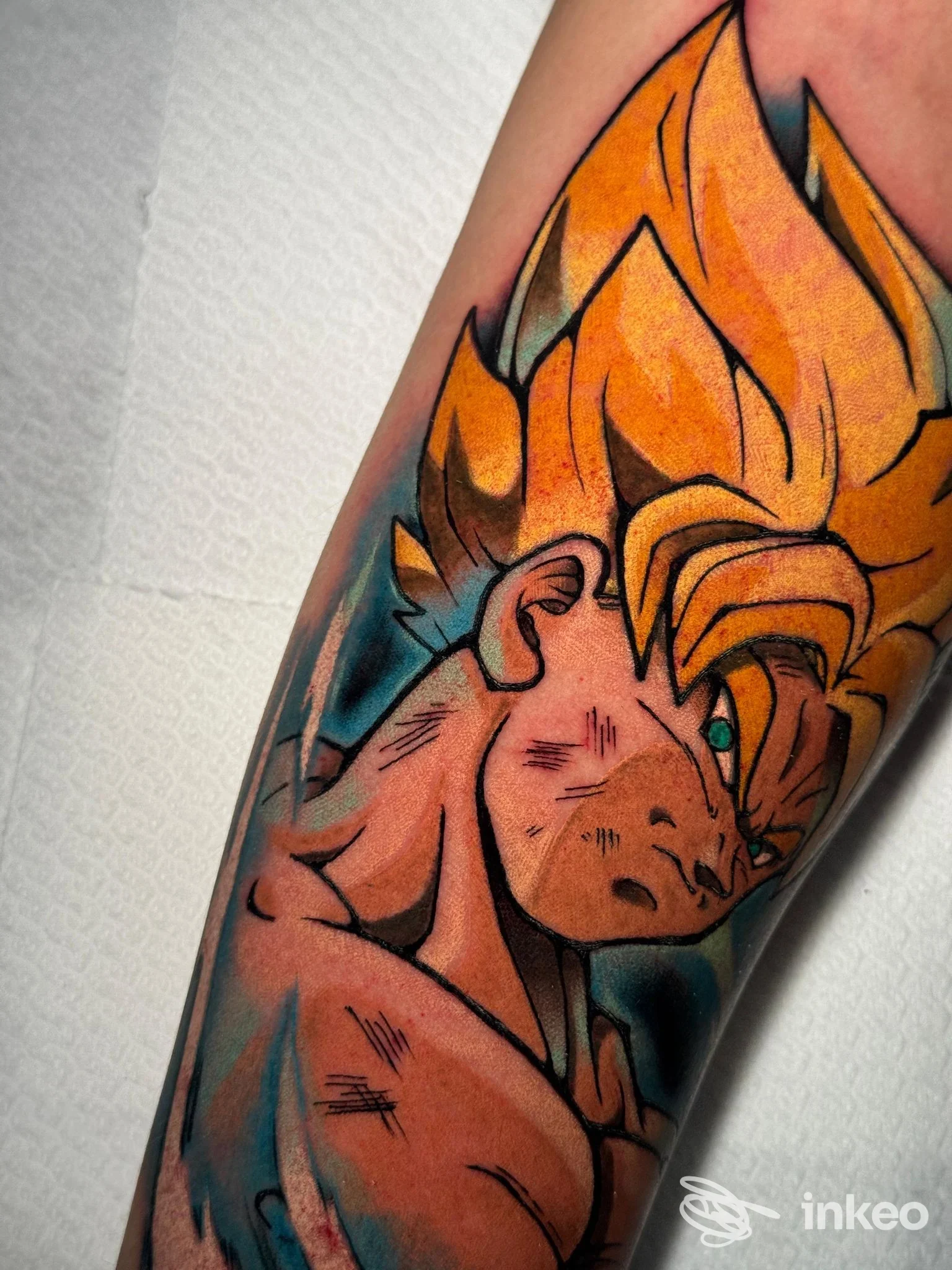 Tattoo colorato raffigurante un personaggio in stile Super Saiyan lungo l'avambraccio, realizzazione su pelle, senza volto visibile.