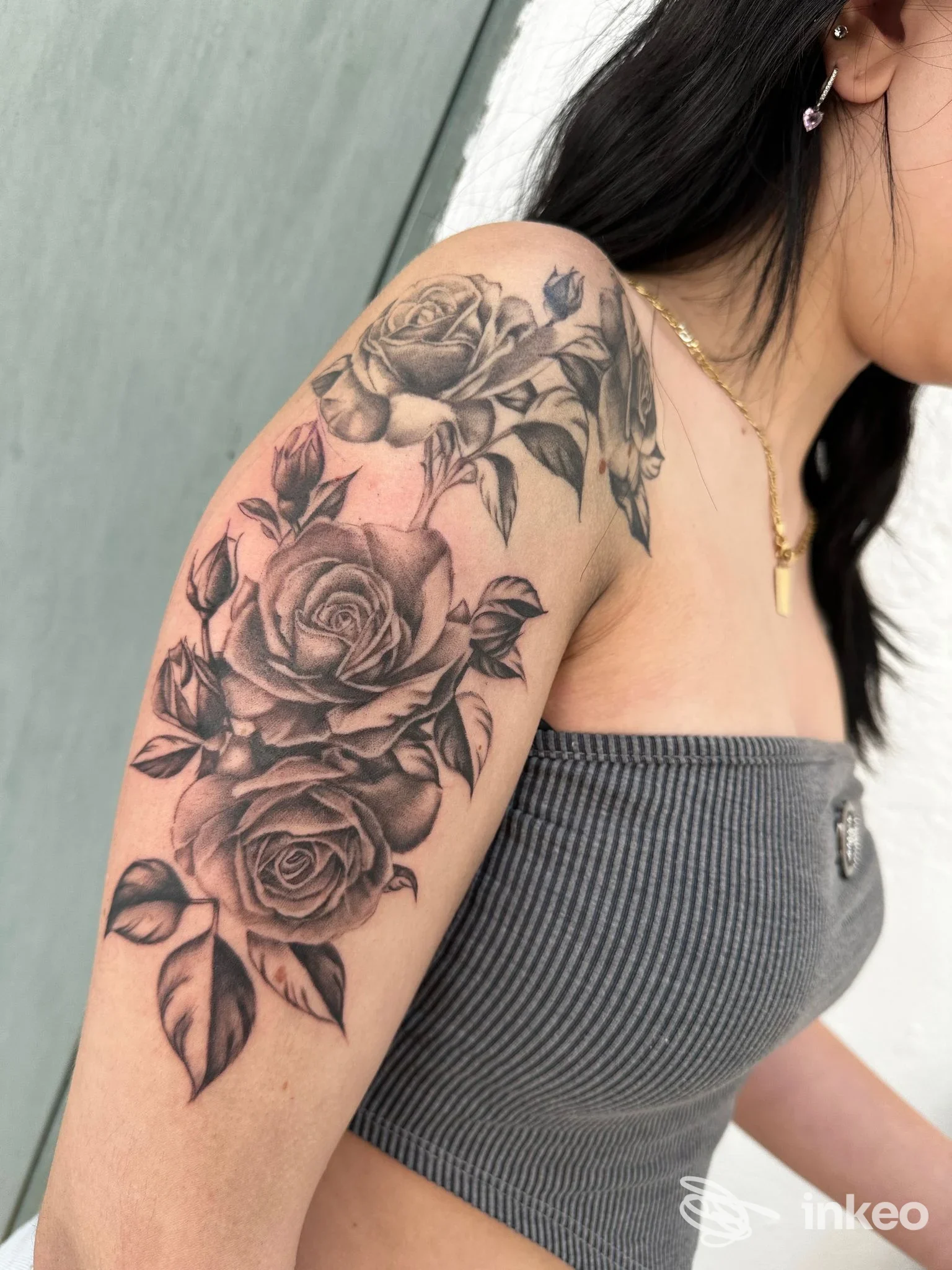 Parte del braccio di una persona con tatuaggio a rose tono nero e grigio su pelle chiara, veduta laterale della spalla, nessun overlay sociale visibile, studio Red Comet Tattoo di Stradella.