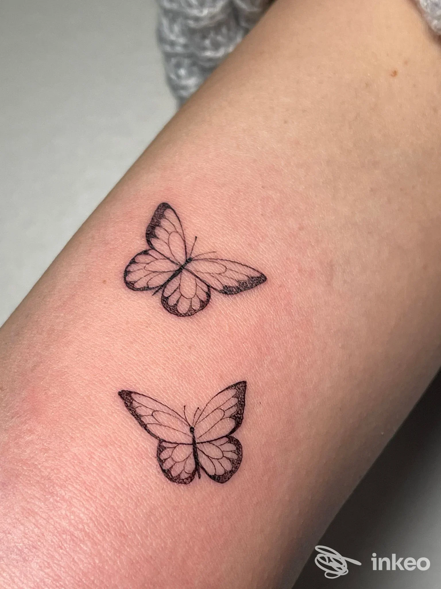 Due piccoli tatuaggi di farfalle disegnati con linee sottili sul braccio, senza testo o elementi di interfaccia visiva, visibili chiaramente.