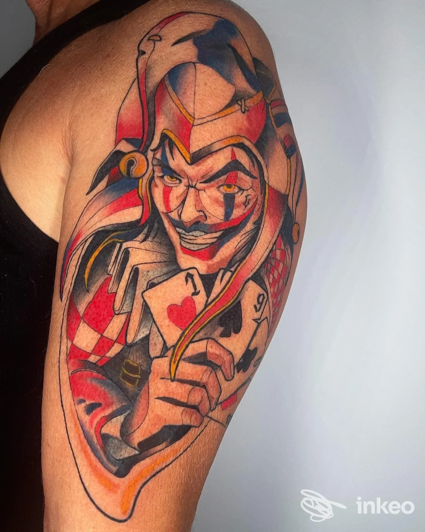 Tatuaggio sul braccio raffigurante un Joker colorato, con cappello e carte, realizzato su pelle, in stile luminoso e vivace.