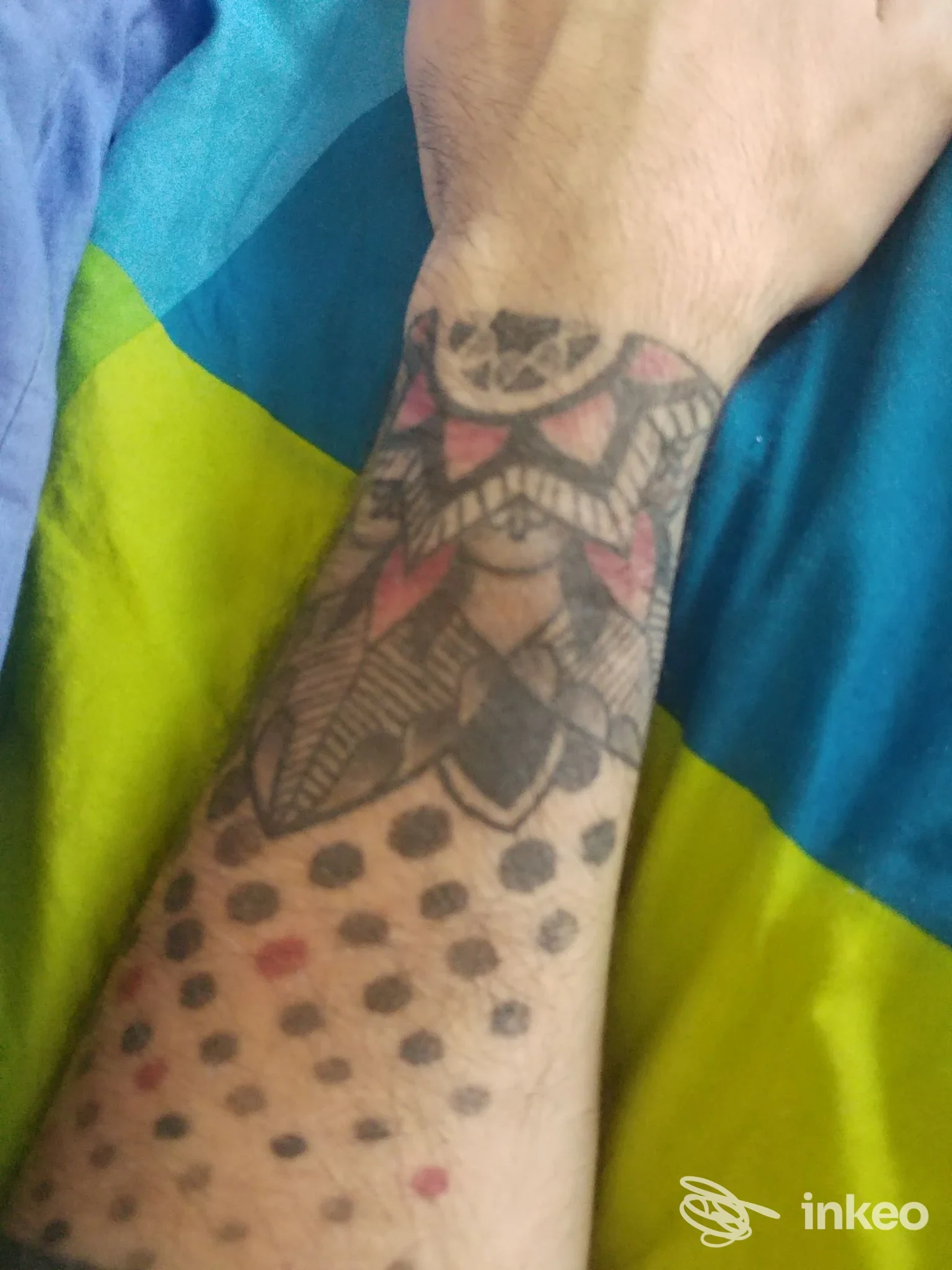 Avambraccio con tatuaggio geometrico e puntini neri sul polso, su sfondo di tessuto colorato; dettaglio chiaro della pelle e dell'inchiostro.