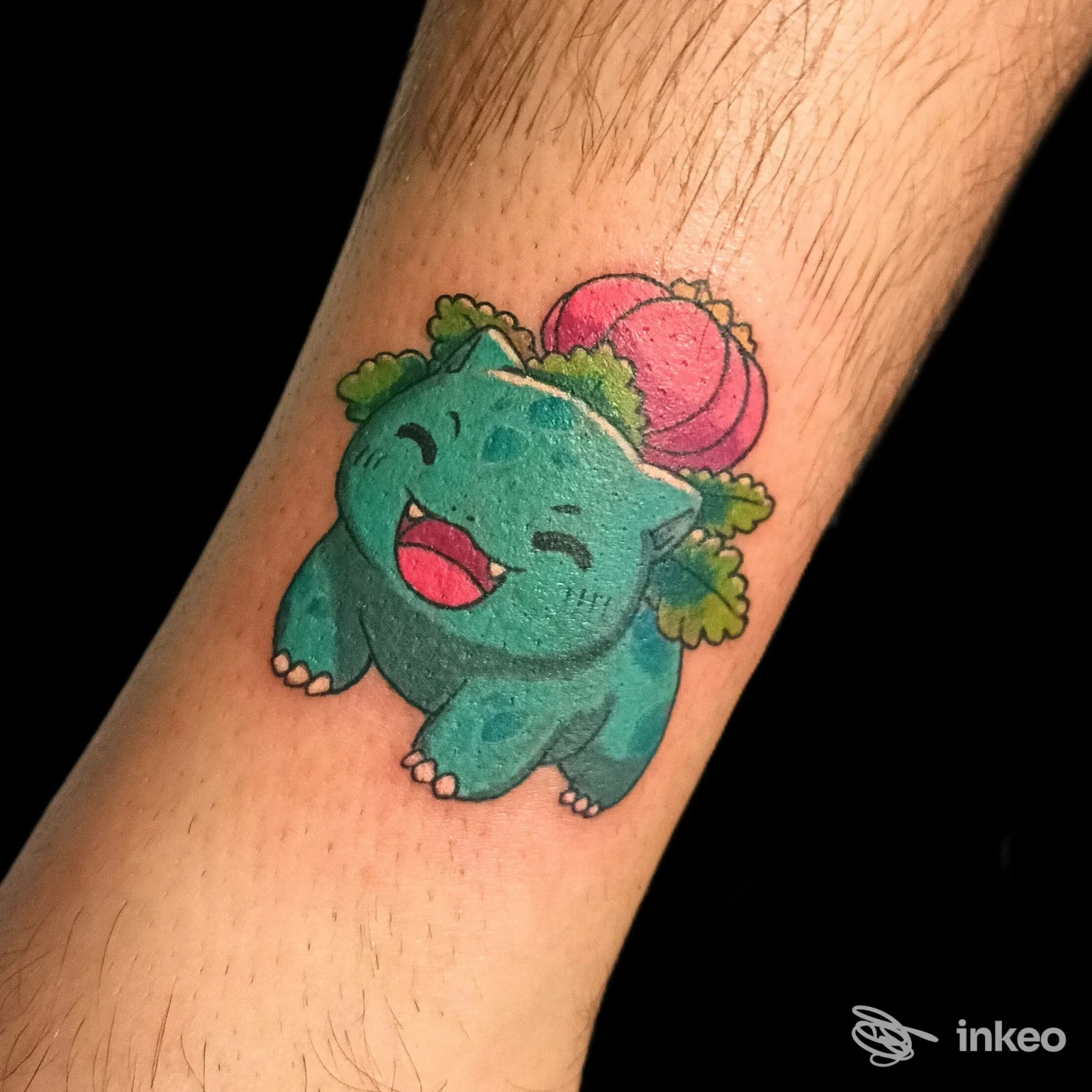 Tattoo su pelle: piccolo dinosauro azzurro felice con un guscio rosa sul dorso, sulla zona dell’avambraccio/polso, colori vivaci.