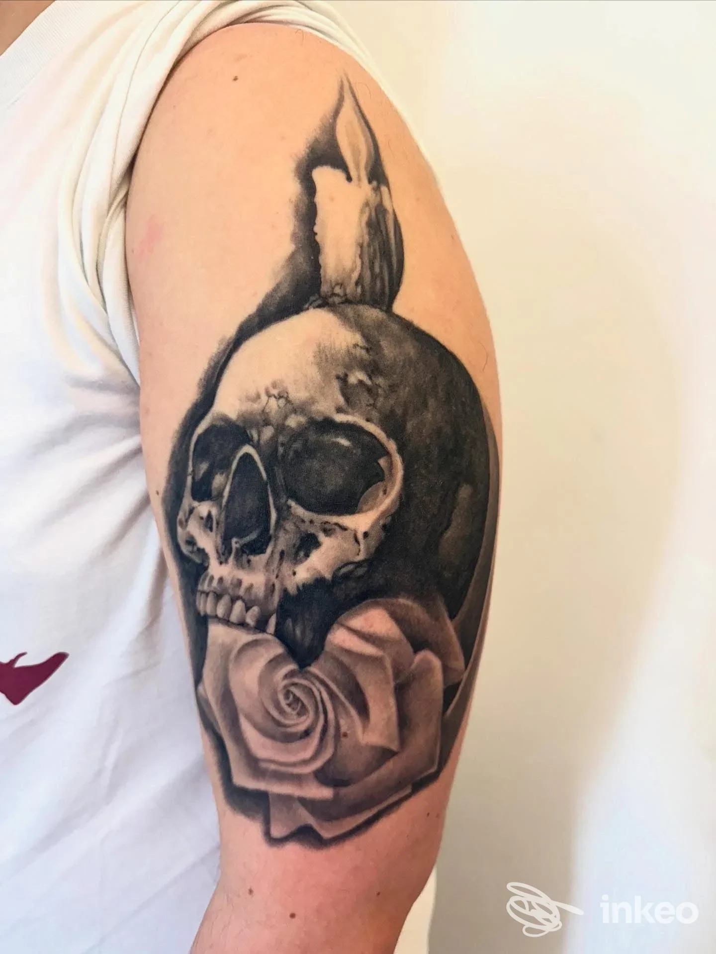 Tattoo a braccio su pelle reale: una testa di scheletro scura combinata con una rosa, eseguita in stile realistico in bianco e nero.