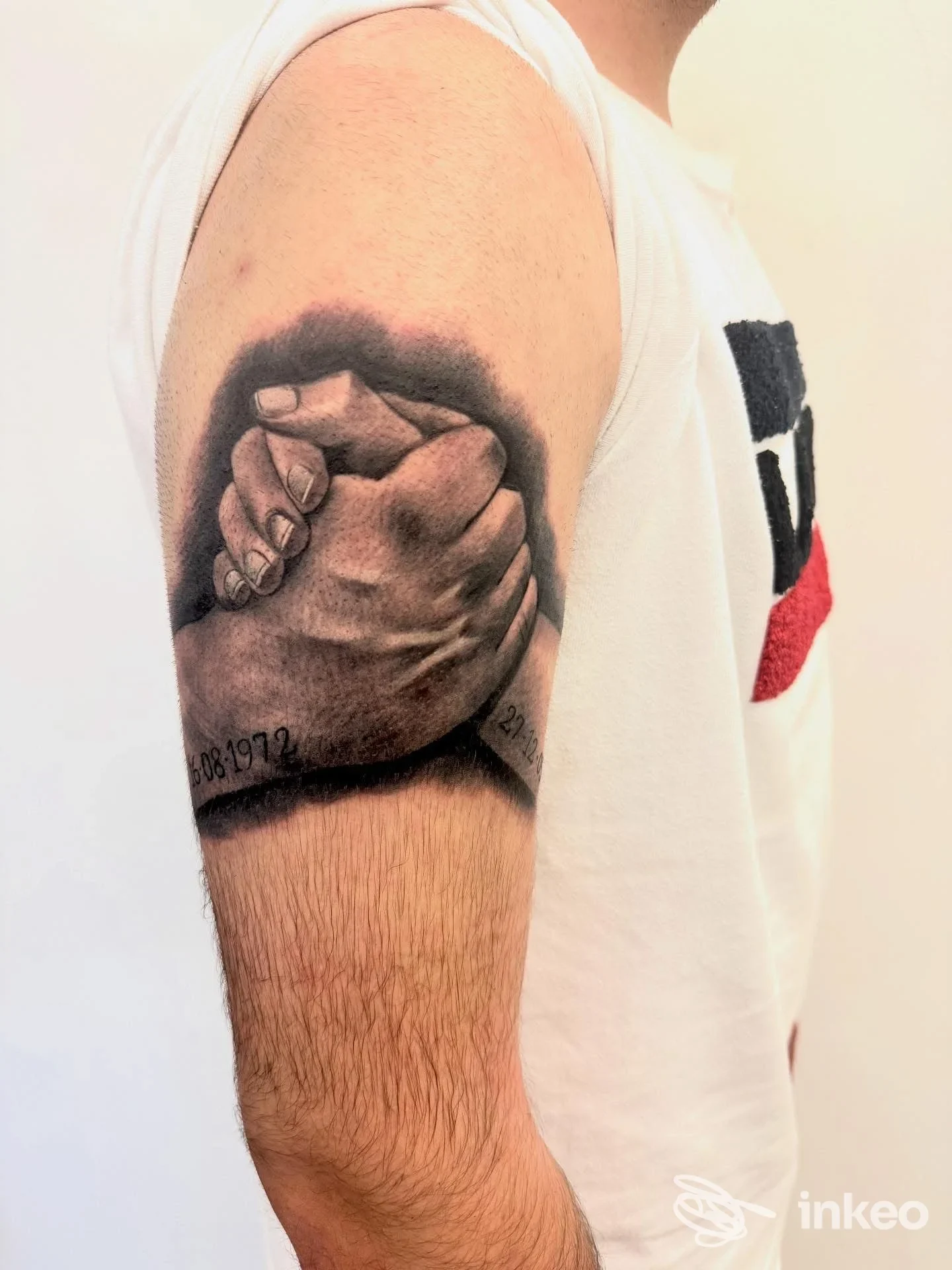 Tatuaggio realistico di due mani che si stringono sull'avambraccio; solo la parte esterna del braccio è visibile, nessun volto.