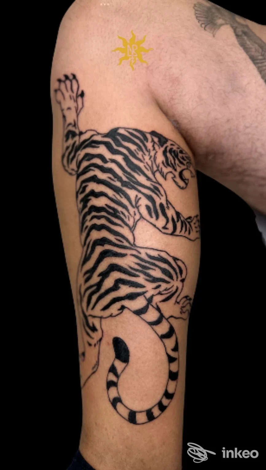 Tattoo su braccio raffigurante tigre in stile linework, con piccolo elemento giallo a forma di sole sulla spalla, senza volto visibile.