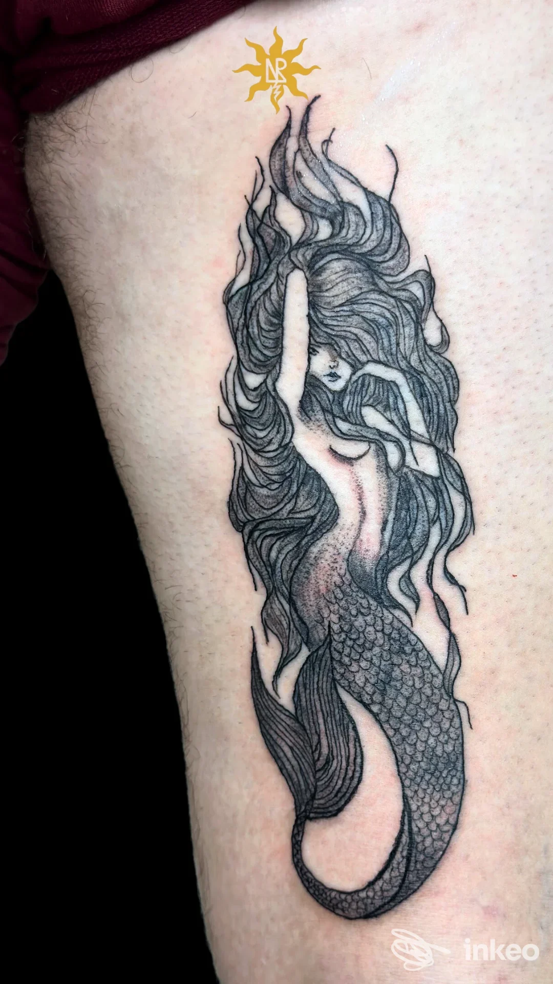 Tattoo su coscia raffigurante una sirena con coda di pesce, disegno in bianco e nero con dettagli nei capelli, sullo sfondo pelle umana.