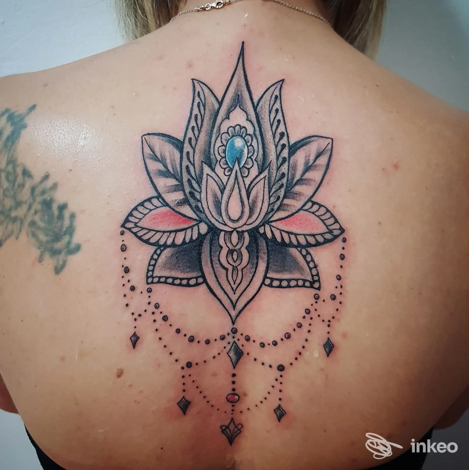 Tattoo sul dorso di una persona: grande lotus/mandala con pendenti e punti decorativi, in stile blackwork e shading grigio.