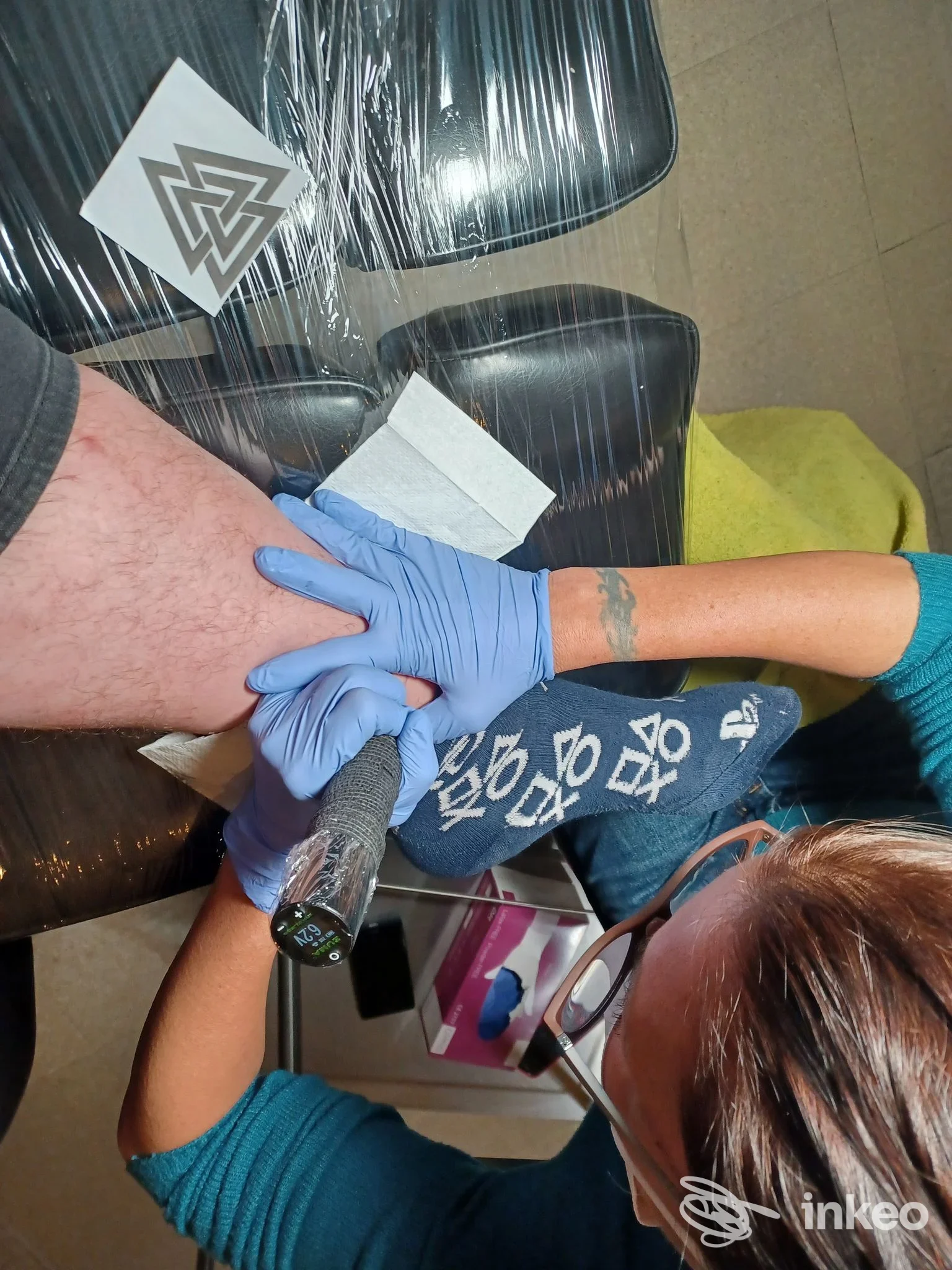 Sessione di tatuaggio in corso su gamba, con guanti blu e macchina per tatuaggio, in studio Camilla Tattoo a Milano.