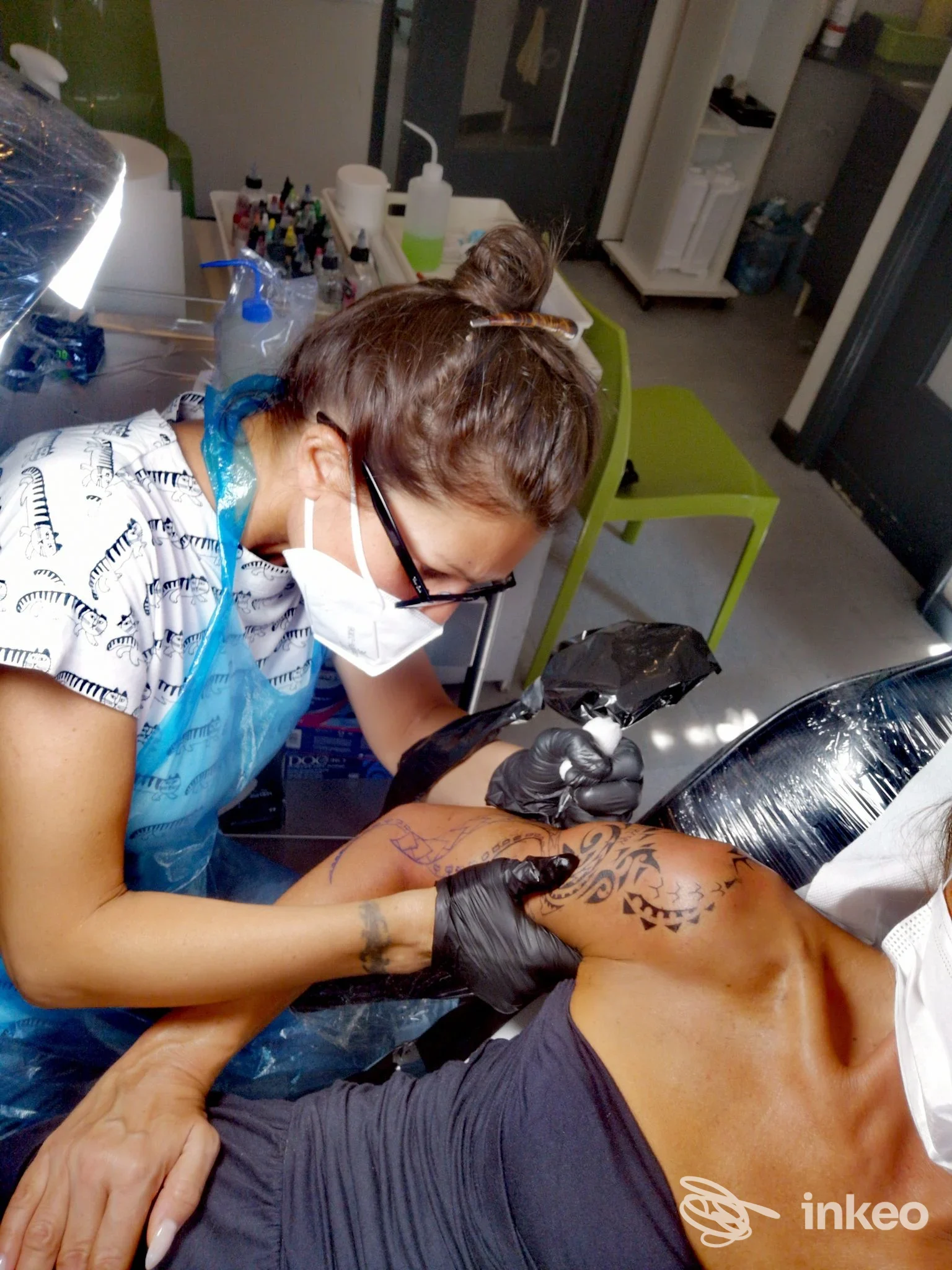 In primo piano si vede una tatuatrice con mascherina e guanti neri che lavora sulladdome di una persona, con aghi e inchiostro visibili durante una sessione di tatuaggio nel studio Camilla Tattoo a Milano.