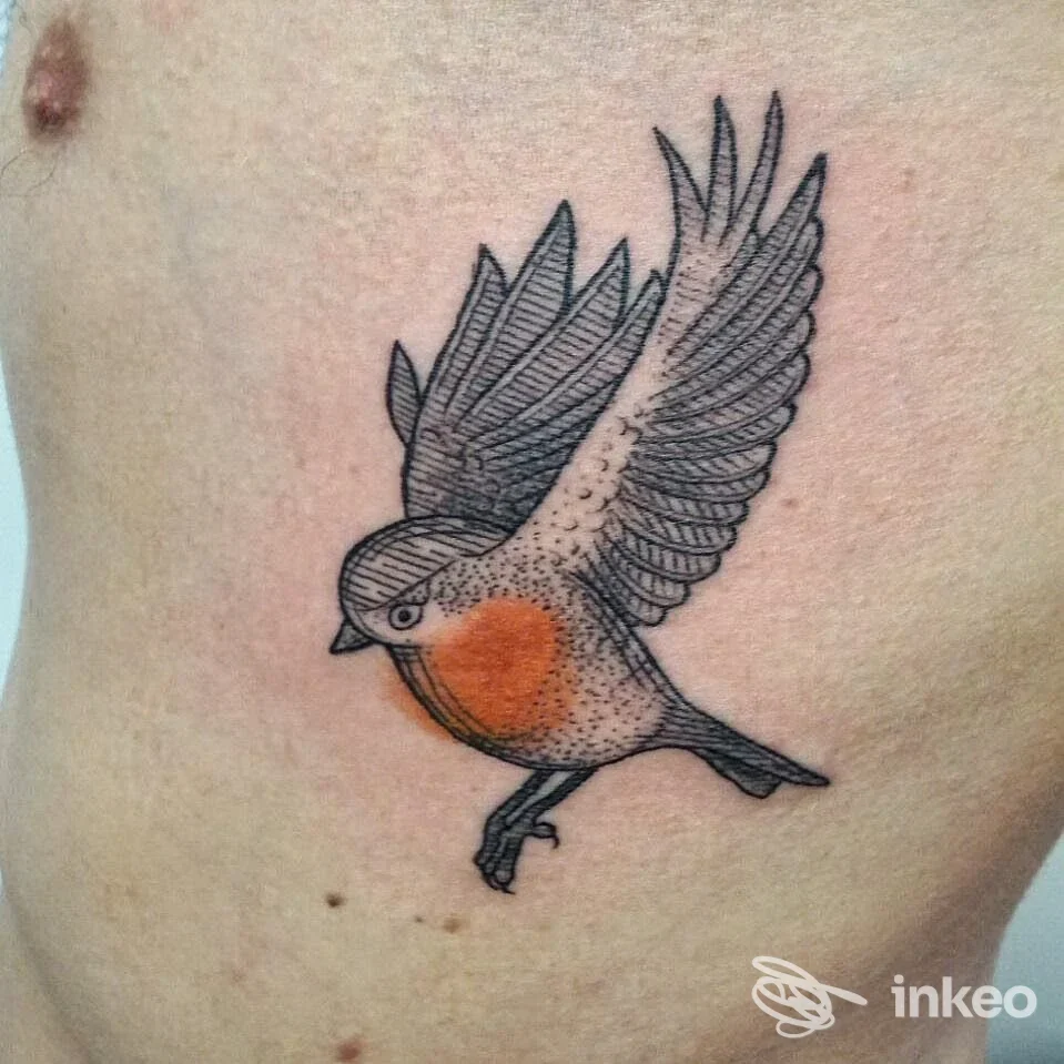Tattoo su pelle raffigurante un uccellino in volo con petto arancione, realizzato sulla pelle del torace sinistro; studio Maneki Tattoo, città non specificata.