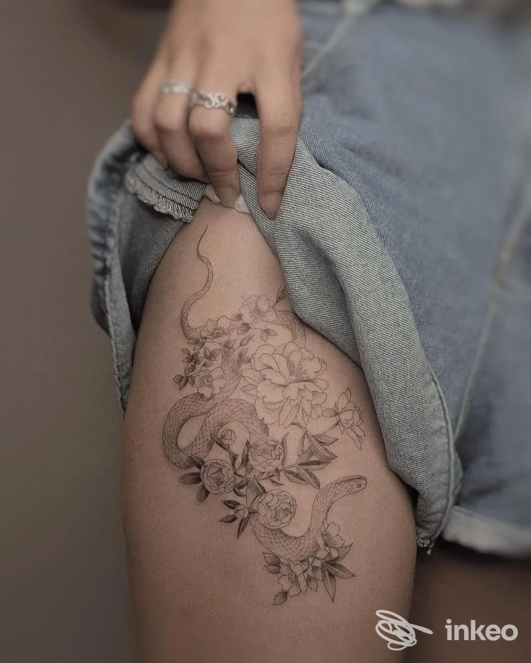 Tattoo floreale e serpente sulla coscia di una persona, ritratto a primo piano su pelle, senza volto visibile.