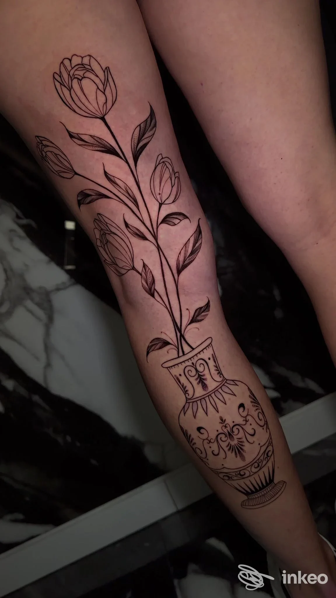 Tattoo visibile sulla gamba: vaso decorativo con bouquet di rose stilizzate, eseguito in nero su pelle, stile line art, studio Tiburón Tattoo, Milano.