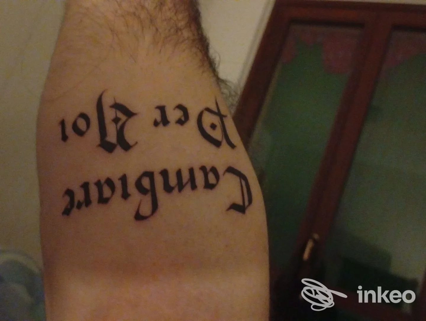 Tattoo visibile sull’avambraccio sinistro, testo in stile gotico, senza volto intero visibile né elementi d’interfaccia sociale.