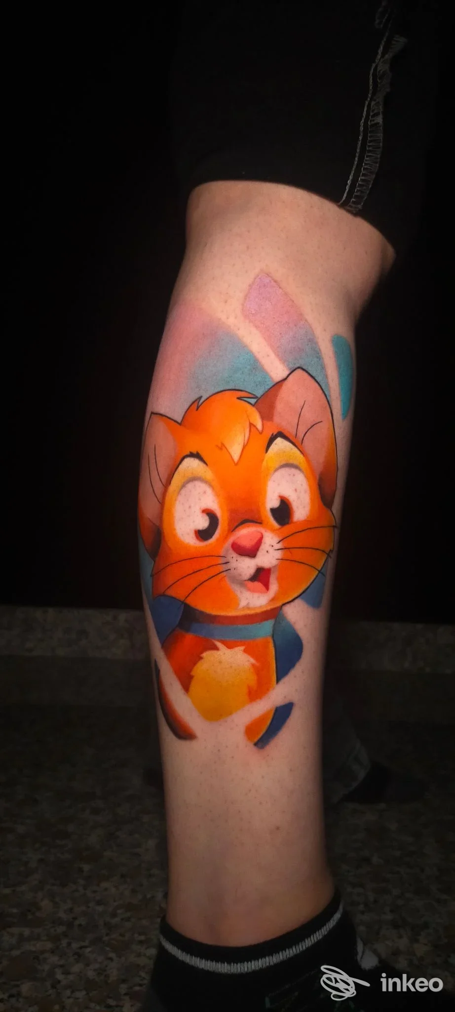 Tattoo colorato di un gatto arancione su gamba, realizzato direttamente sulla pelle; lo sfondo è scuro, l’immagine mostra una singola inquadratura del tattoo.