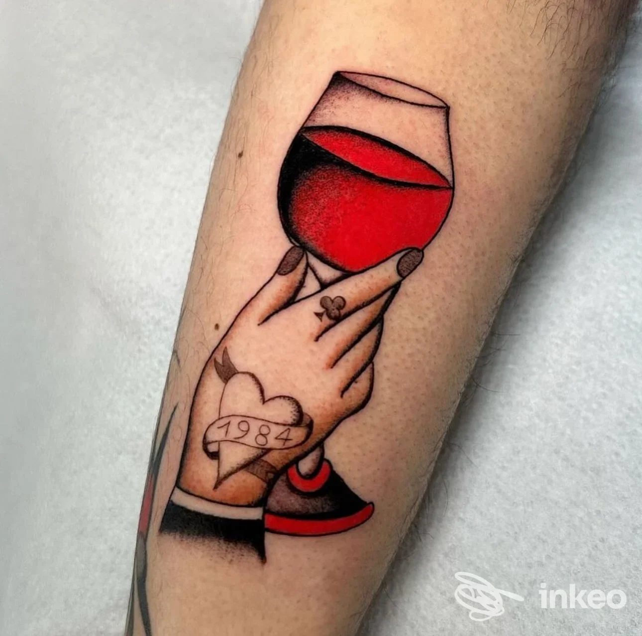 Tattoo raffigurante due mani che sostengono un calice di vino rosso, con un cuore tatuato sul polso; stile colorato con contorni netti sull’avambraccio.