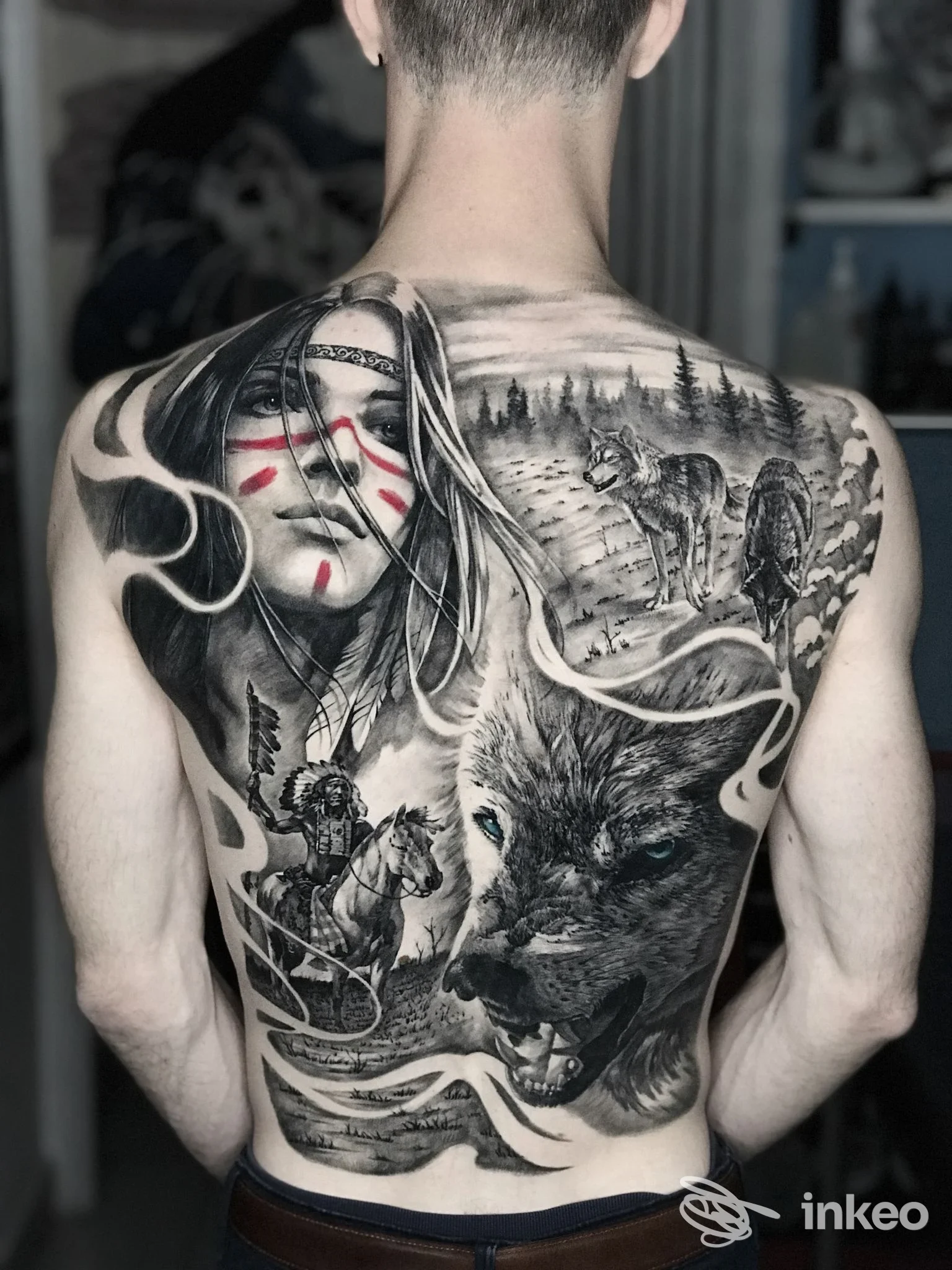Tattoo realistico in bianco e nero sulla schiena: ritratto di donna con maschera, lupi e paesaggio boschivo, con elementi sinuosi che attraversano la pelle.