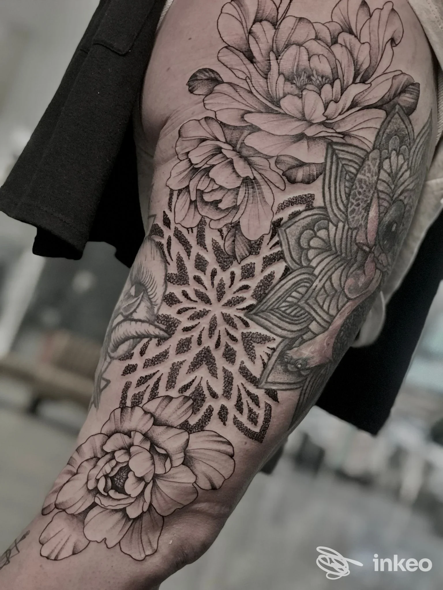 Tattoo floreale in bianco e nero su braccio, con motivi floreali intricati e disegno ornamentale, visibile in primo piano.